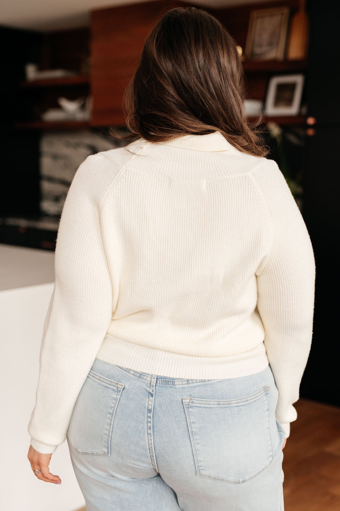 A women's cream cropped sweater made of lightweight sweater knit fabric, featuring a V-neckline with a shawl collar, long sleeves, and a faux wrap design.