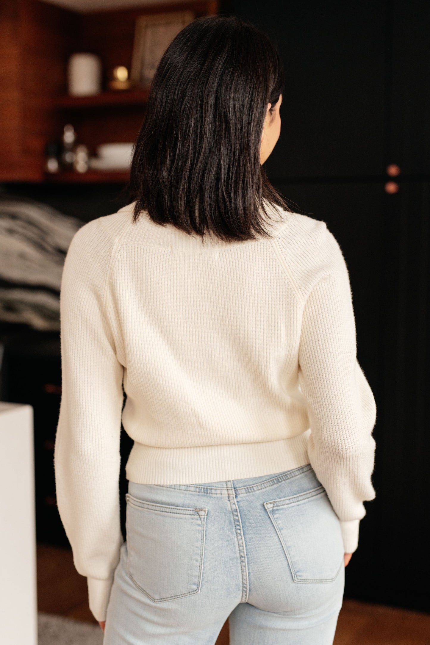 A women's cream cropped sweater made of lightweight sweater knit fabric, featuring a V-neckline with a shawl collar, long sleeves, and a faux wrap design.