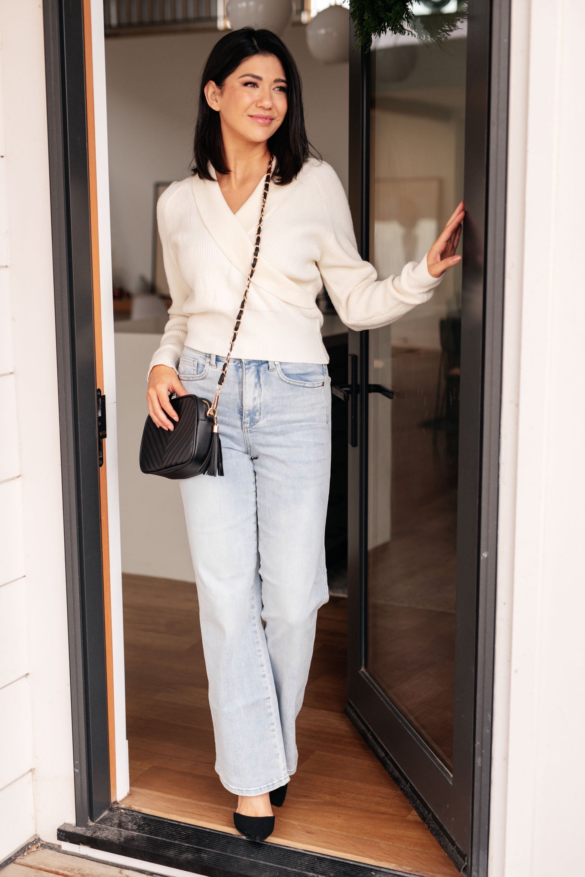 A women's cream cropped sweater made of lightweight sweater knit fabric, featuring a V-neckline with a shawl collar, long sleeves, and a faux wrap design.