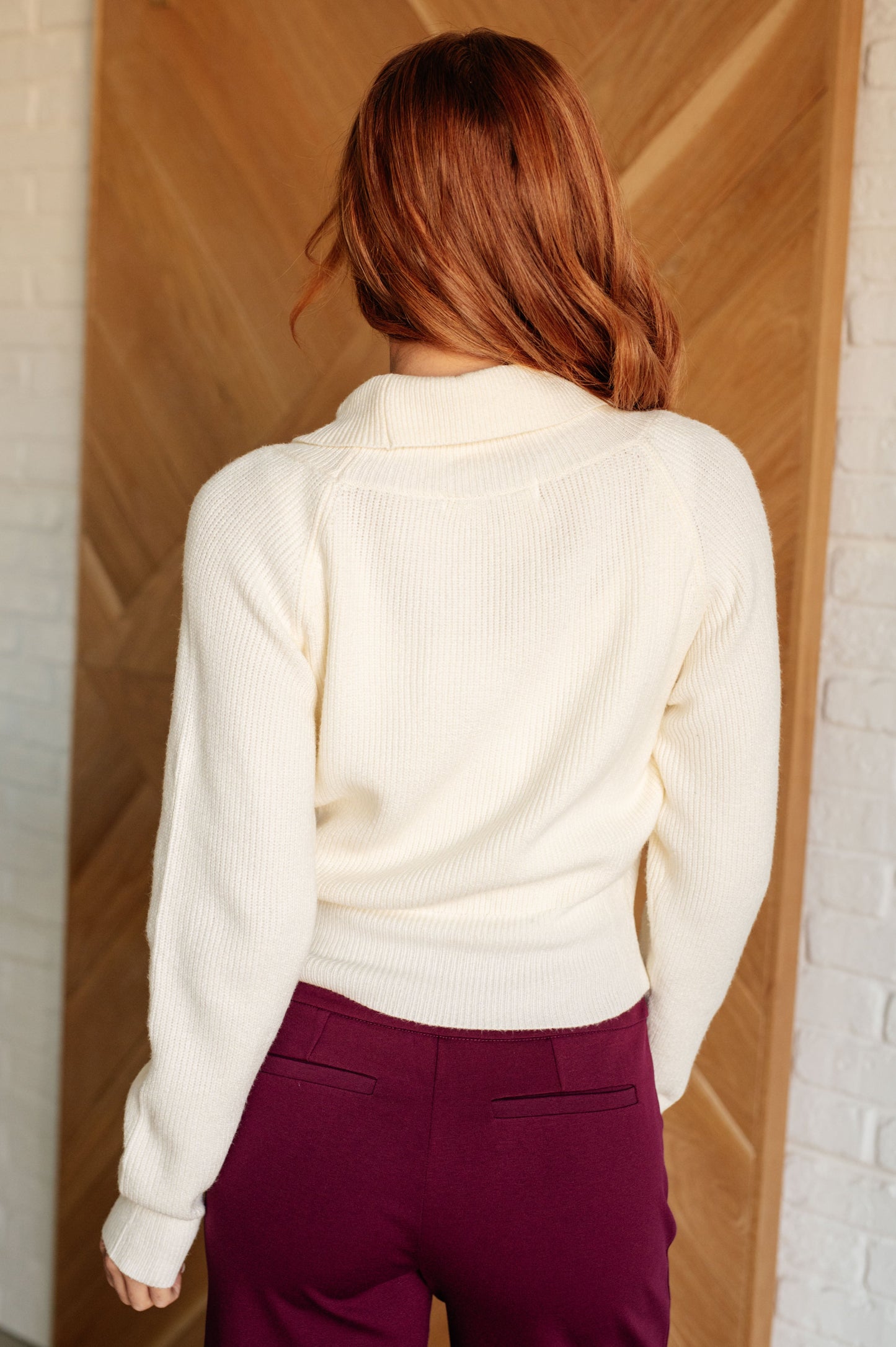 A women's cream cropped sweater made of lightweight sweater knit fabric, featuring a V-neckline with a shawl collar, long sleeves, and a faux wrap design.