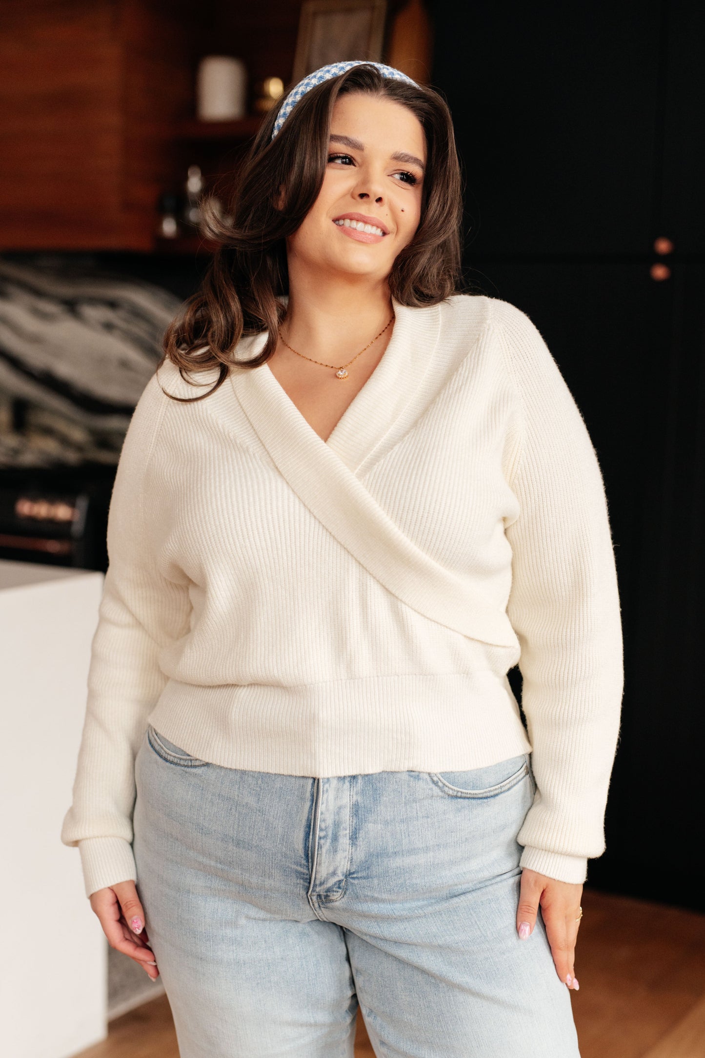 A women's cream cropped sweater made of lightweight sweater knit fabric, featuring a V-neckline with a shawl collar, long sleeves, and a faux wrap design.