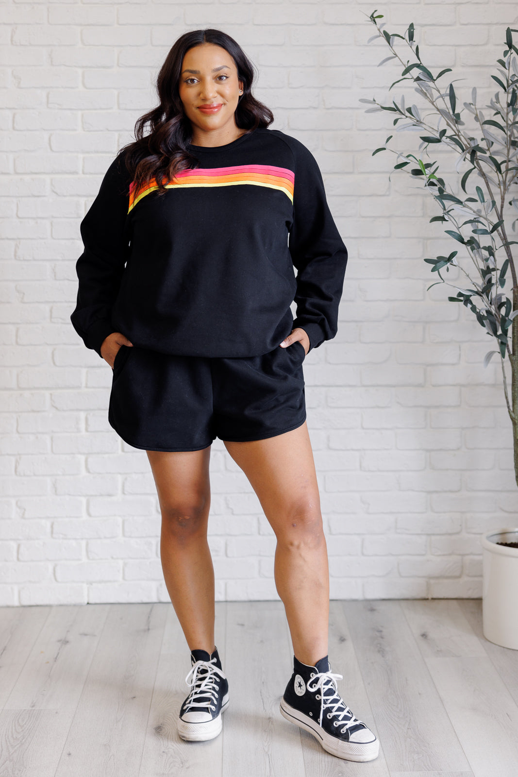 Black retro rainbow knit set includes a top with raglan sleeves and a round neckline, paired with shorts featuring banded ribbed details, an elastic waistline, and functional side pockets. Top and bottom have a contrast striped applique.