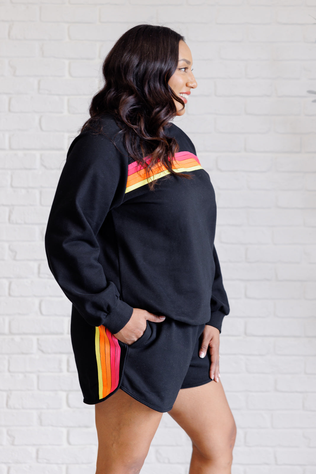 Black retro rainbow knit set includes a top with raglan sleeves and a round neckline, paired with shorts featuring banded ribbed details, an elastic waistline, and functional side pockets. Top and bottom have a contrast striped applique.