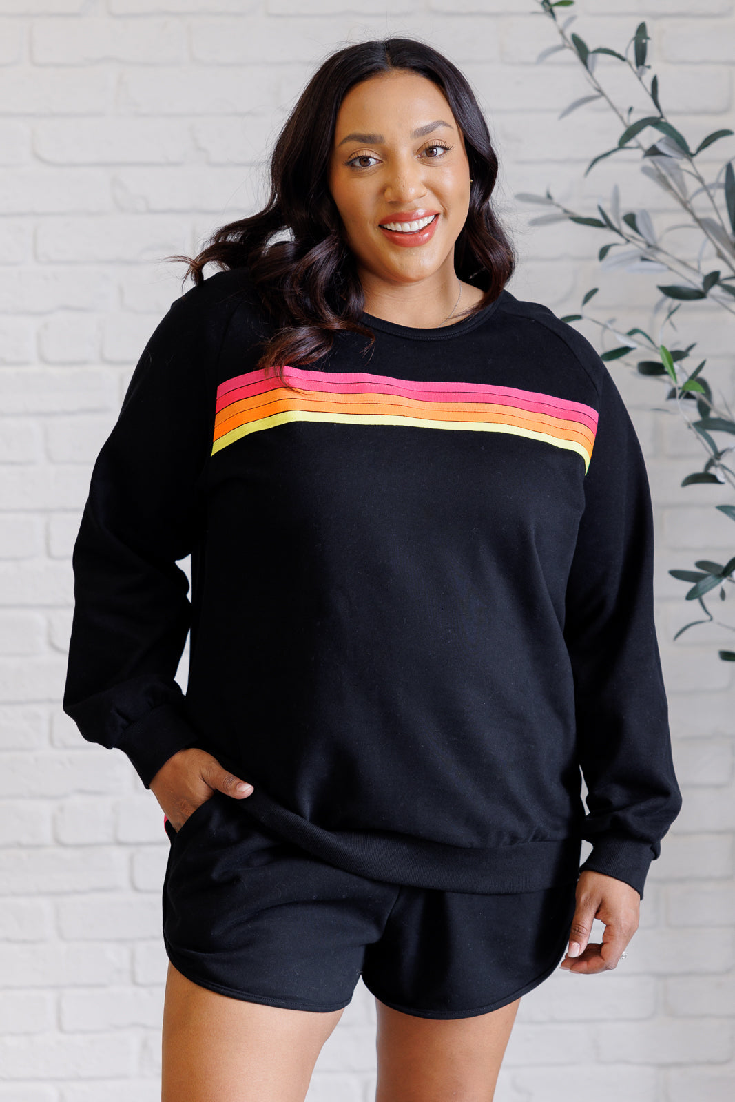 Black retro rainbow knit set includes a top with raglan sleeves and a round neckline, paired with shorts featuring banded ribbed details, an elastic waistline, and functional side pockets. Top and bottom have a contrast striped applique.