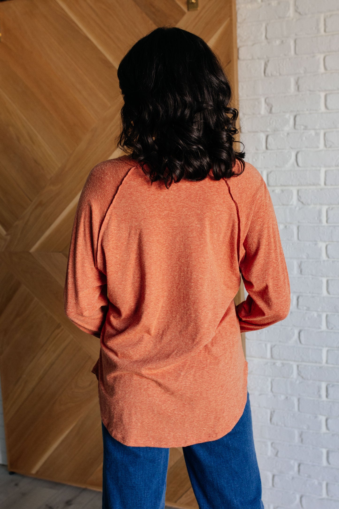 Pumpkin-colored long sleeve top with raglan sleeves, exposed seams, thumb hole cuffs, and scooped hemline.