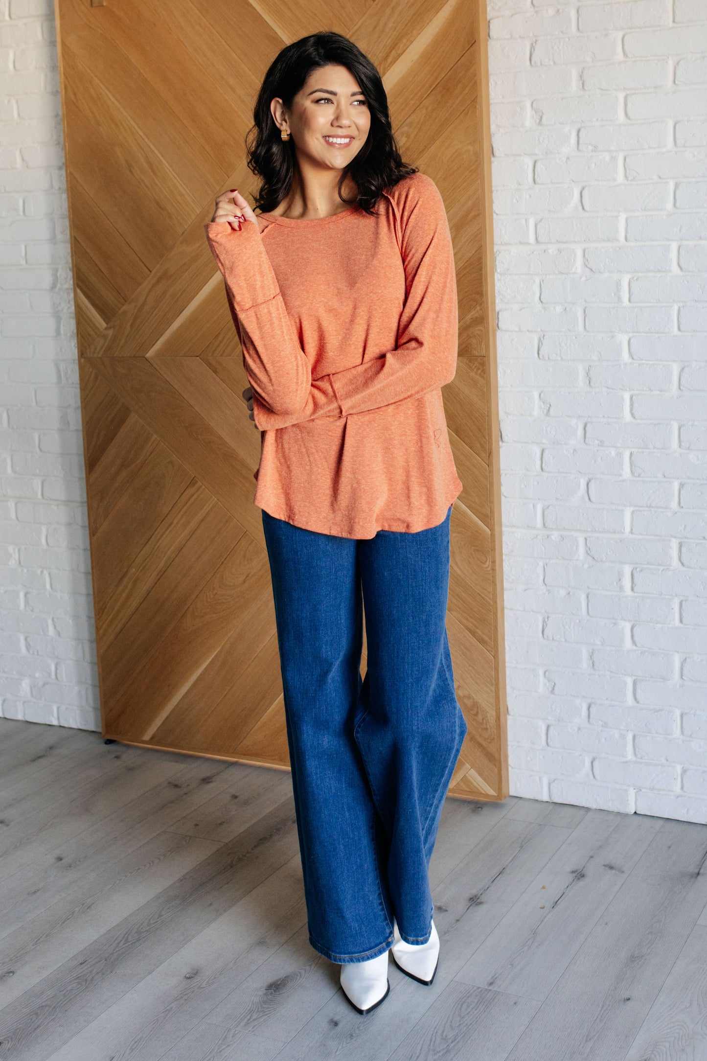 Pumpkin-colored long sleeve top with raglan sleeves, exposed seams, thumb hole cuffs, and scooped hemline.