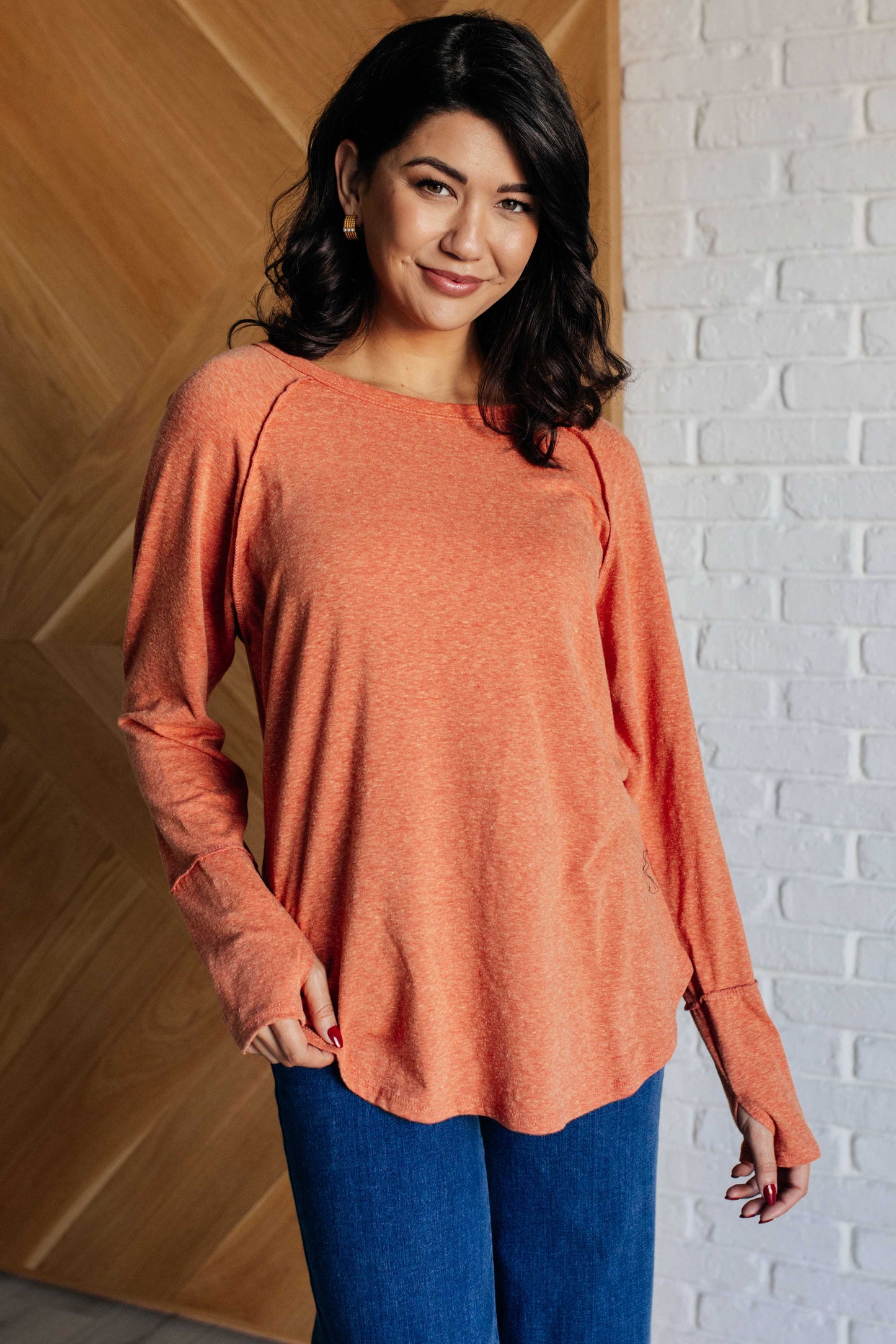 Pumpkin-colored long sleeve top with raglan sleeves, exposed seams, thumb hole cuffs, and scooped hemline.