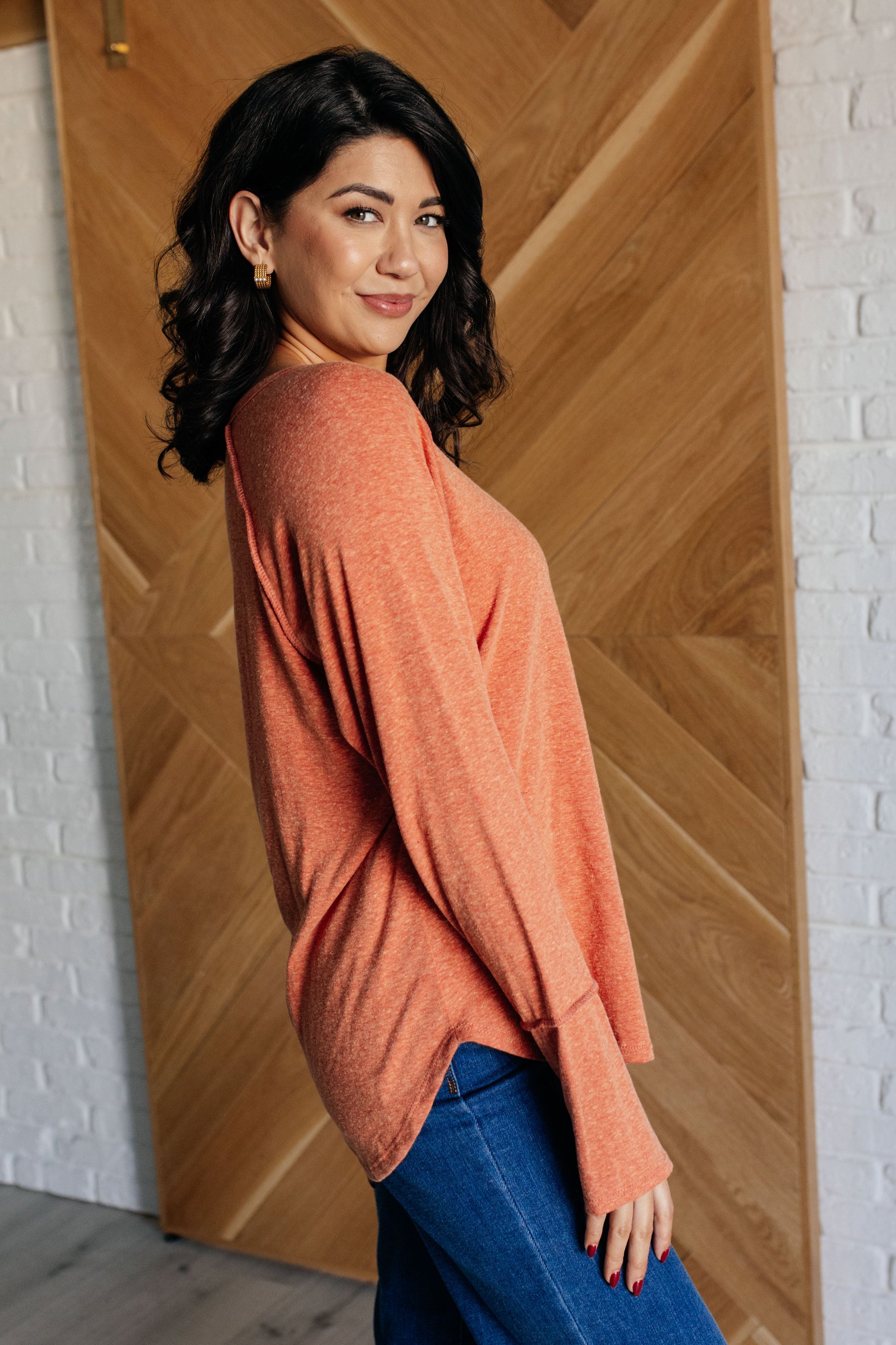 Pumpkin-colored long sleeve top with raglan sleeves, exposed seams, thumb hole cuffs, and scooped hemline.