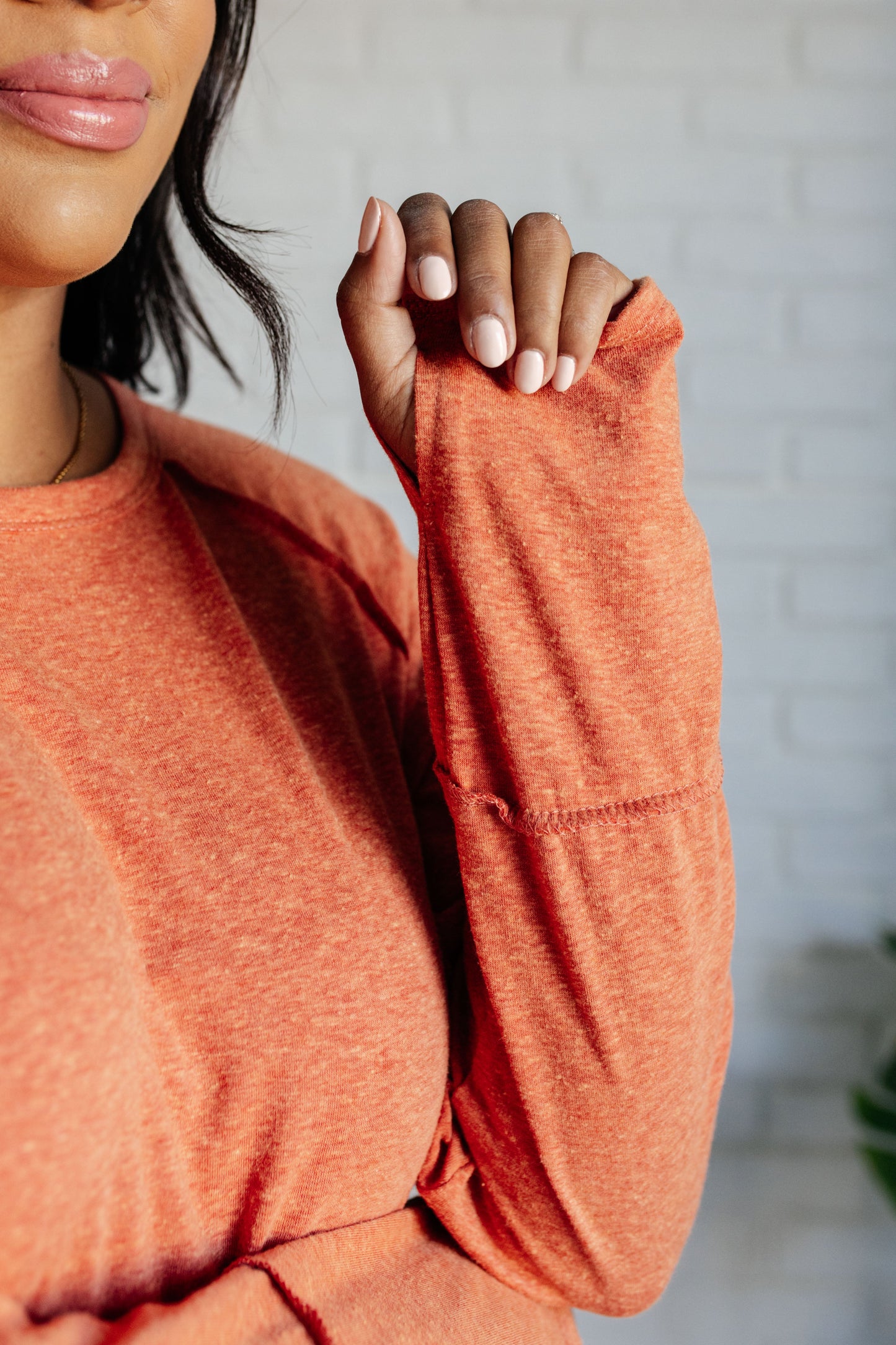 Pumpkin-colored long sleeve top with raglan sleeves, exposed seams, thumb hole cuffs, and scooped hemline.