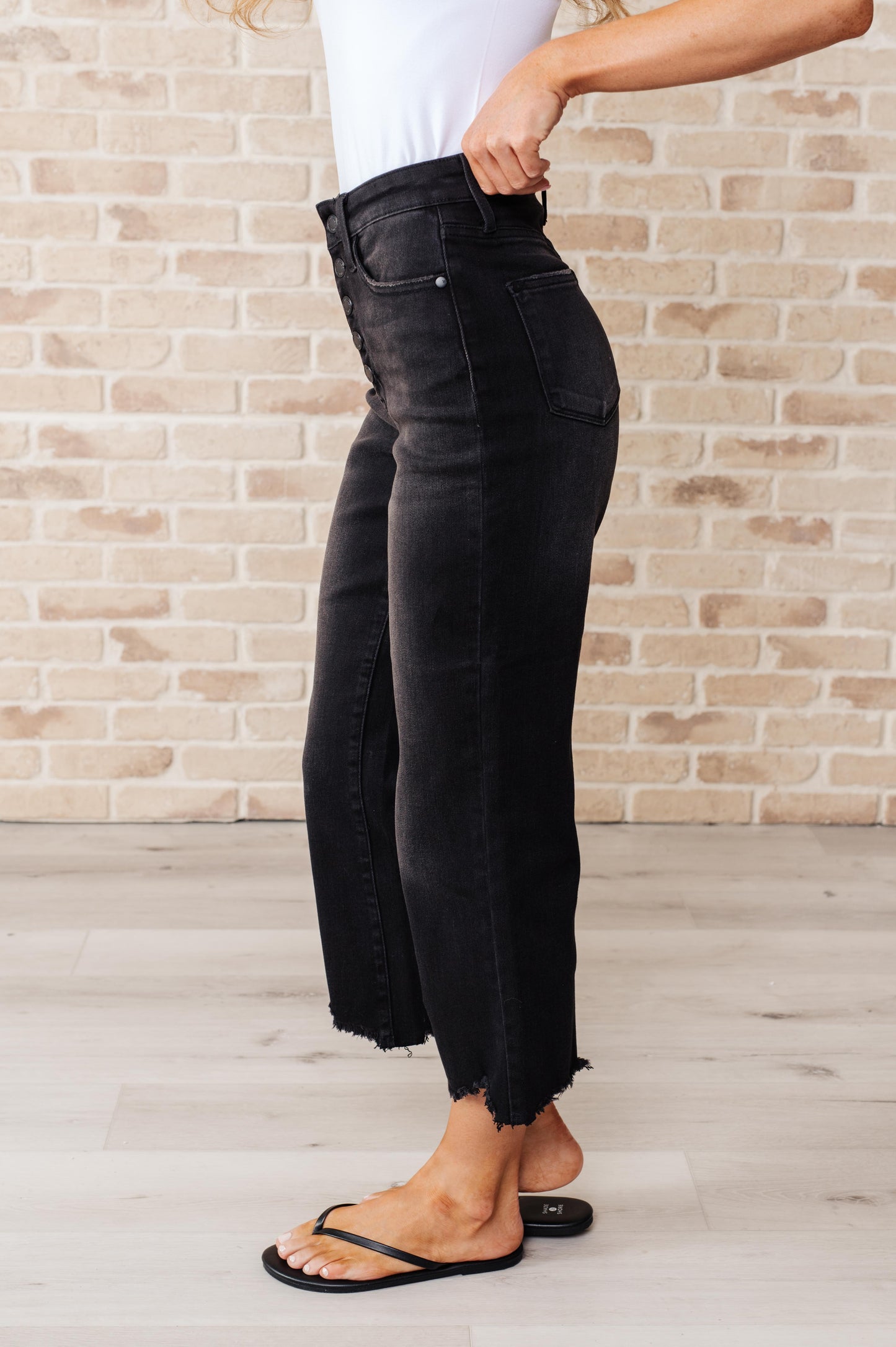 Black garment dyed wide leg crop jeans with high rise, raw hem, and button fly closure.