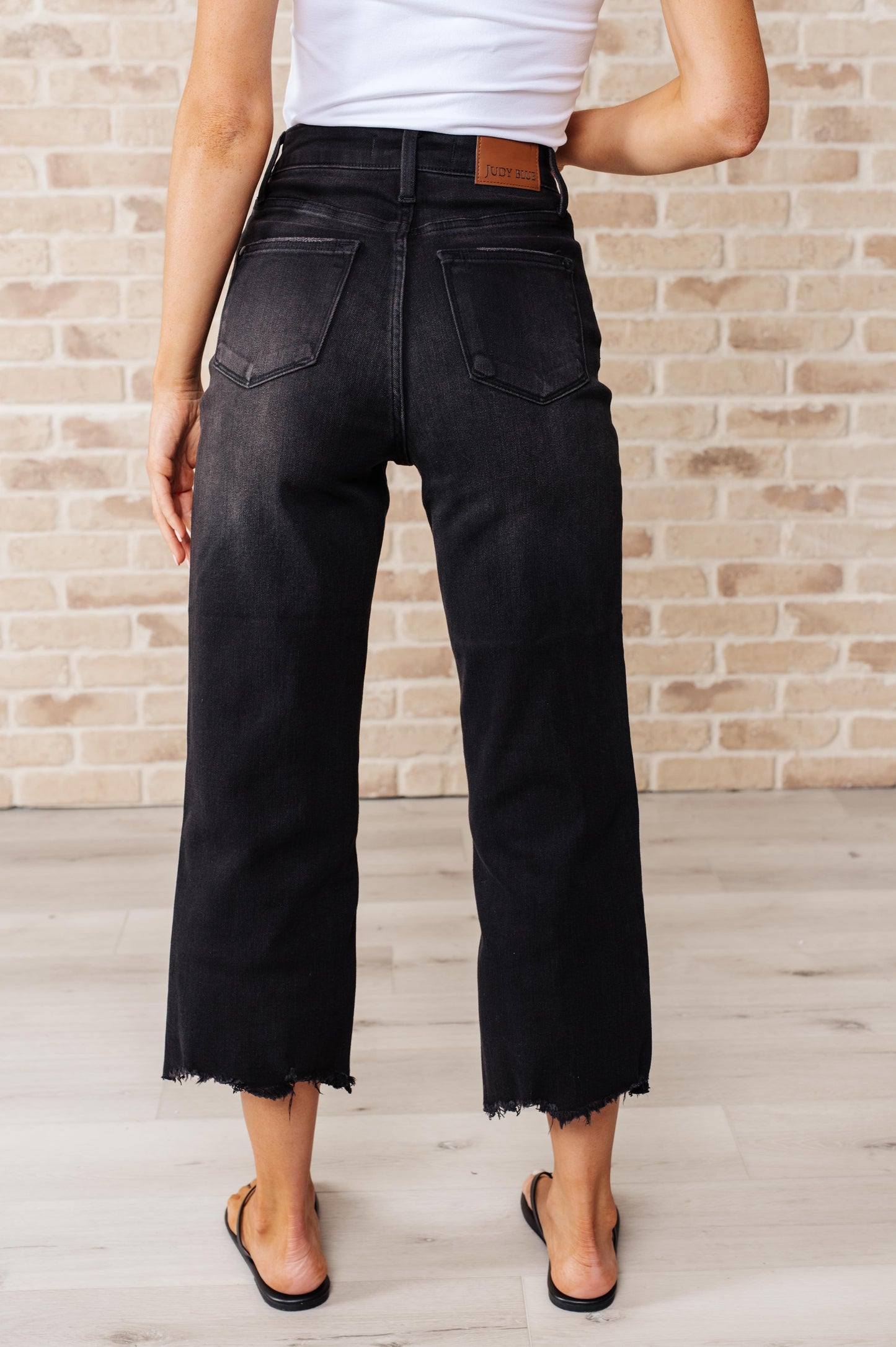 Black garment dyed wide leg crop jeans with high rise, raw hem, and button fly closure.