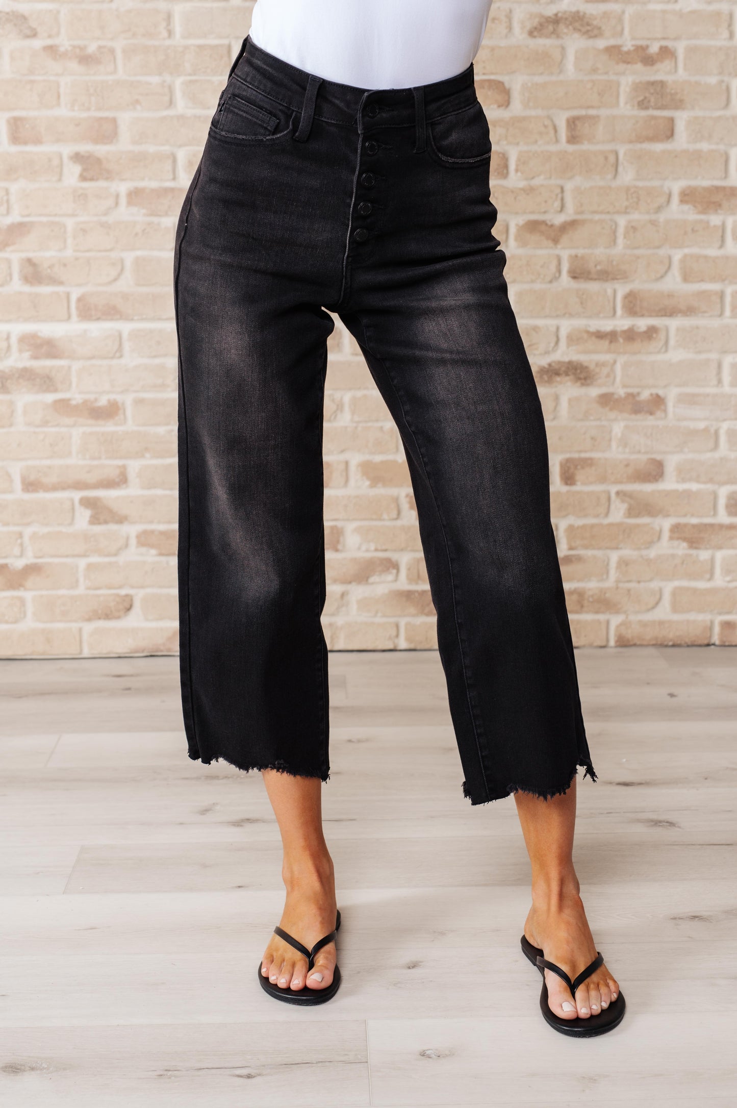 Black garment dyed wide leg crop jeans with high rise, raw hem, and button fly closure.