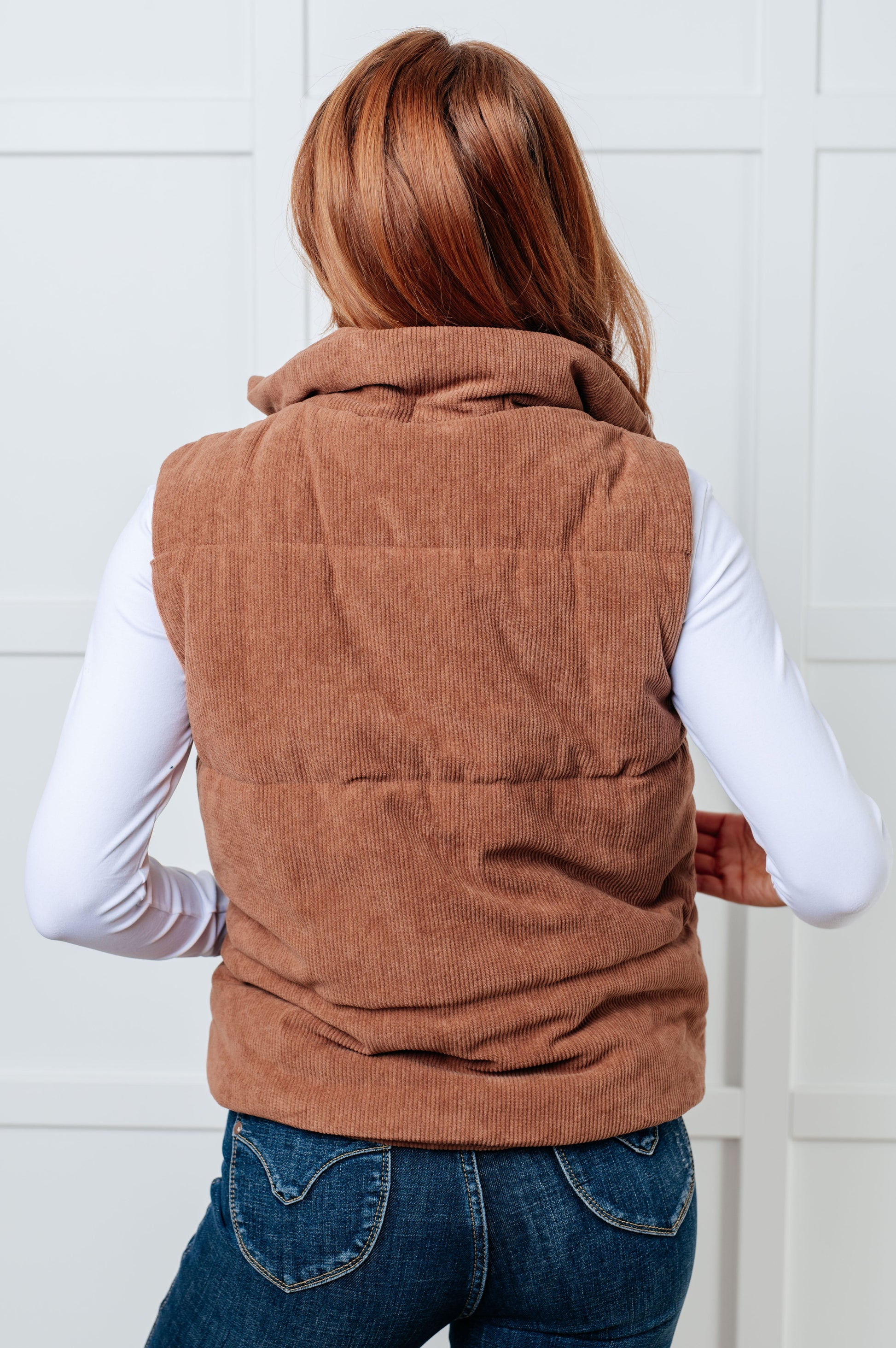 Brown corduroy puffer vest with a high-collared neckline, sleeveless design, full front zipper closure, functional welt pockets, and fully lined interior.