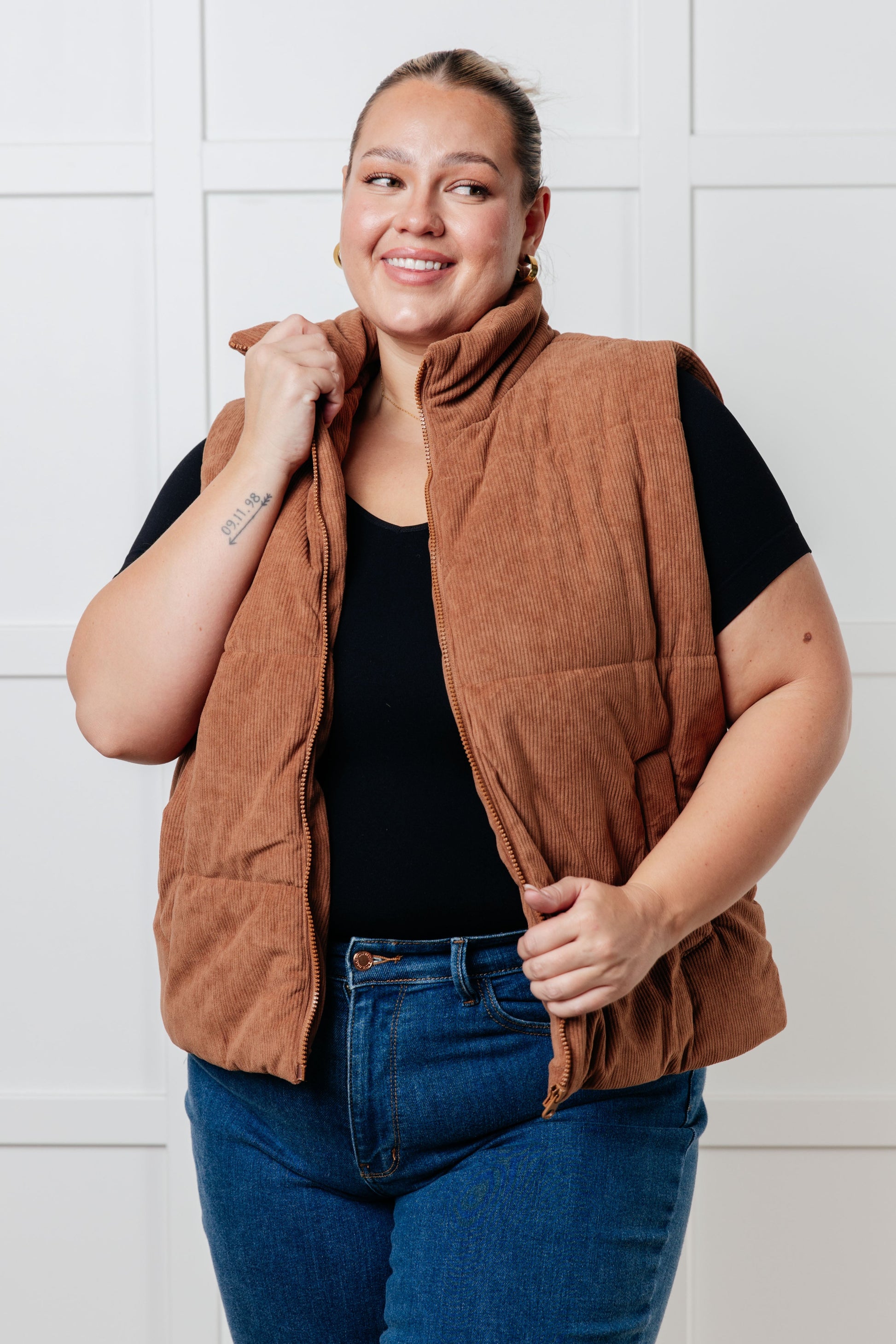 Brown corduroy puffer vest with a high-collared neckline, sleeveless design, full front zipper closure, functional welt pockets, and fully lined interior.