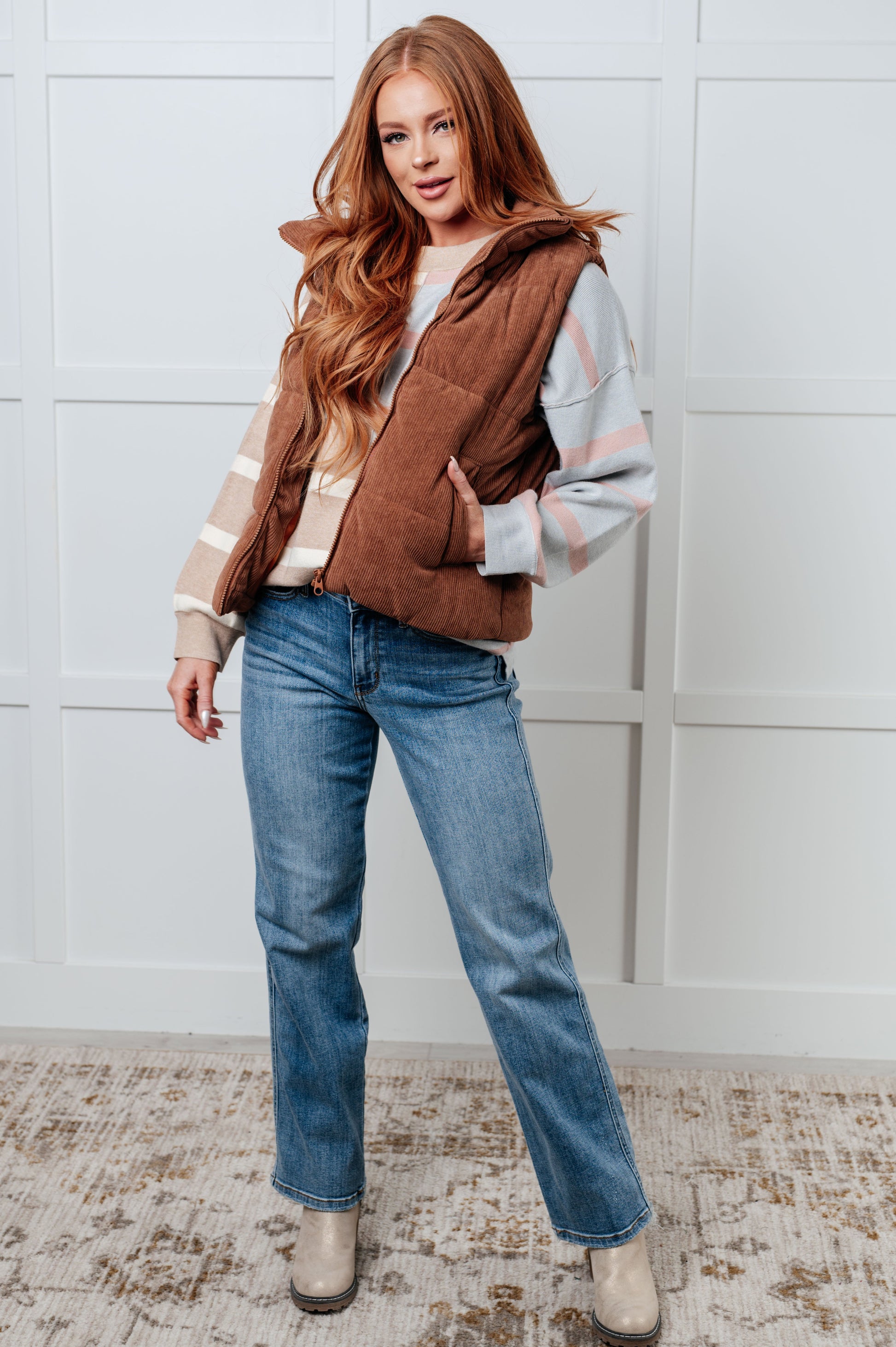 Brown corduroy puffer vest with a high-collared neckline, sleeveless design, full front zipper closure, functional welt pockets, and fully lined interior.