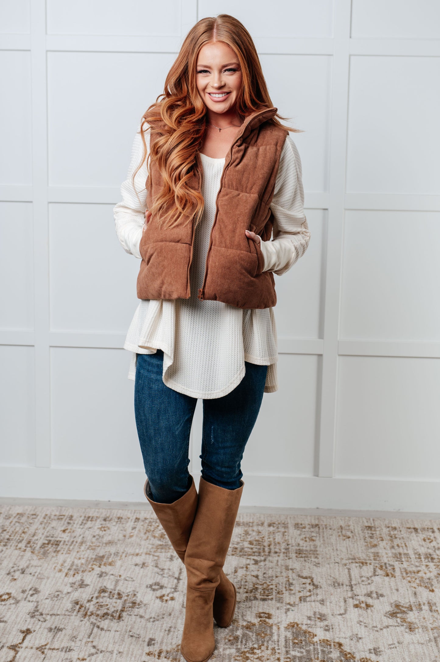 Brown corduroy puffer vest with a high-collared neckline, sleeveless design, full front zipper closure, functional welt pockets, and fully lined interior.