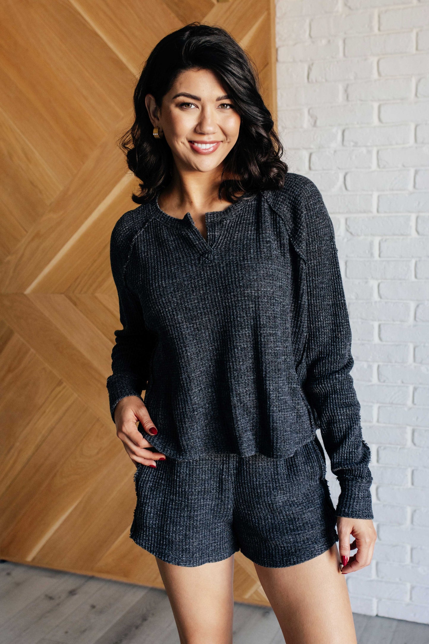 Black waffle knit pullover and shorts set featuring a henley-style neckline, long sleeves, elastic waist, functional side pockets and raw edge details.