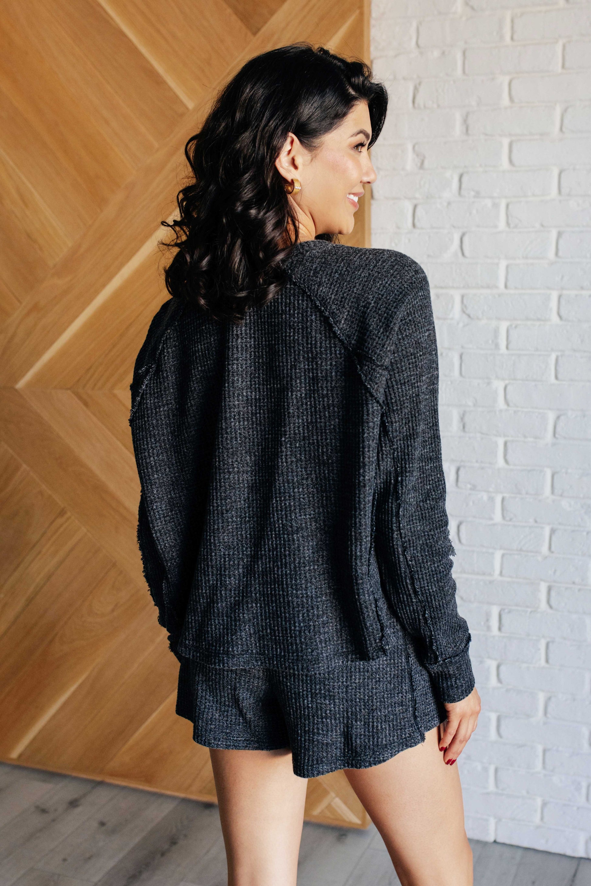 Black waffle knit pullover and shorts set featuring a henley-style neckline, long sleeves, elastic waist, functional side pockets and raw edge details.