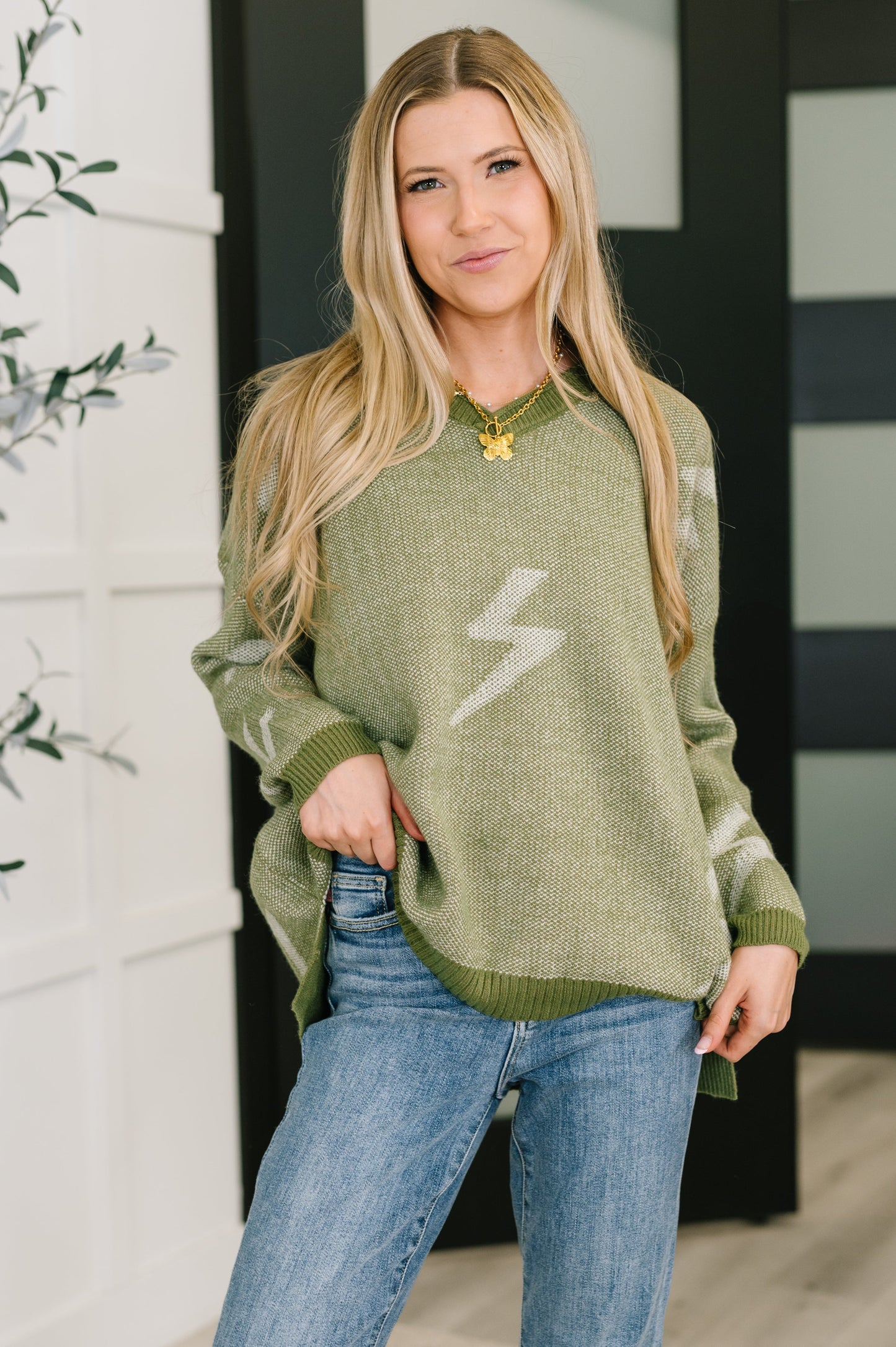 Model wearing Shoni V-Neck Sweater in Olive with lightning bolt pattern and drop shoulders.