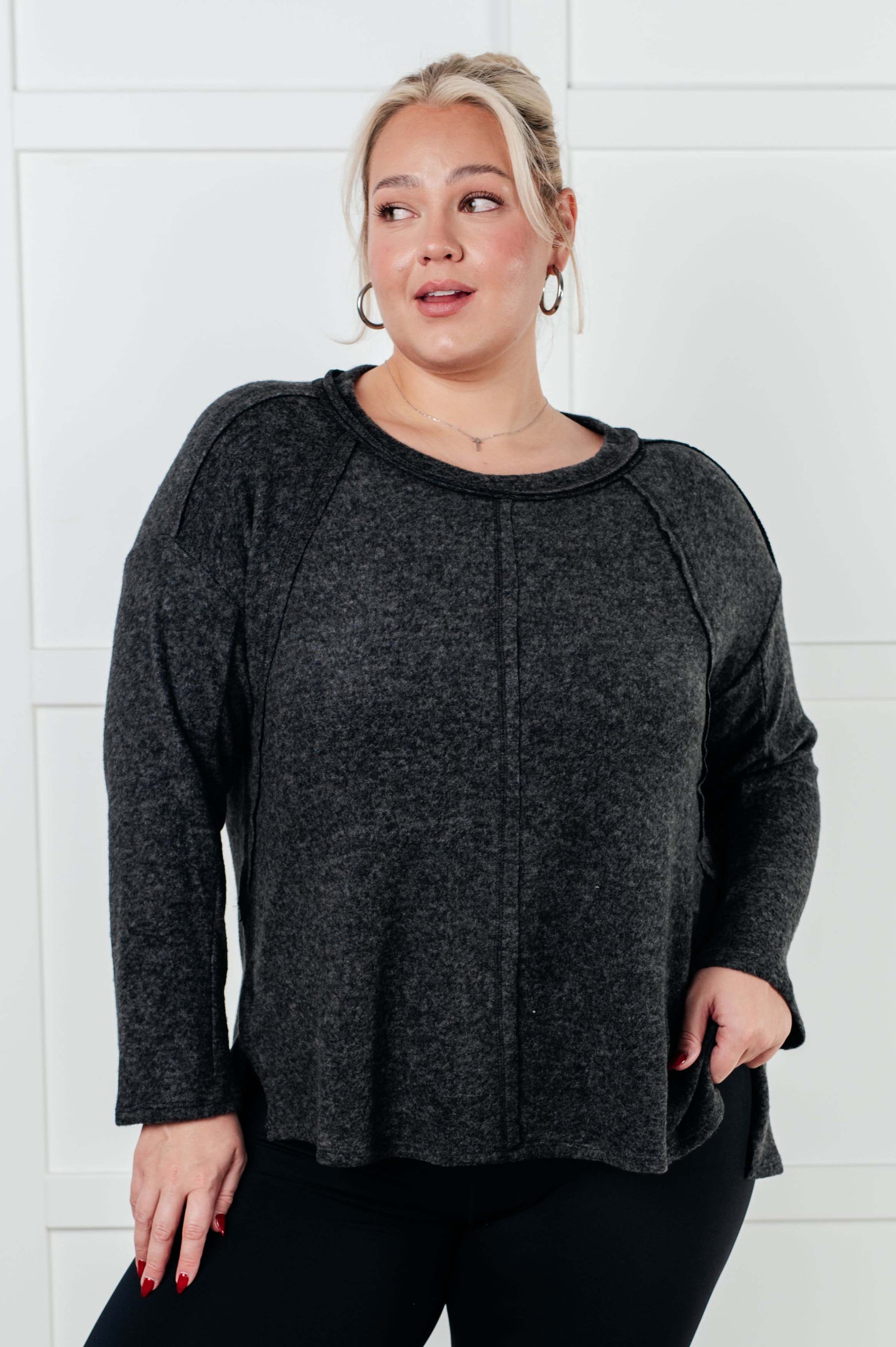 Women's Symmer Brushed Hacci Sweater in Black featuring a round neckline, drop shoulders, stepped hemline, side slits, and raw seams.