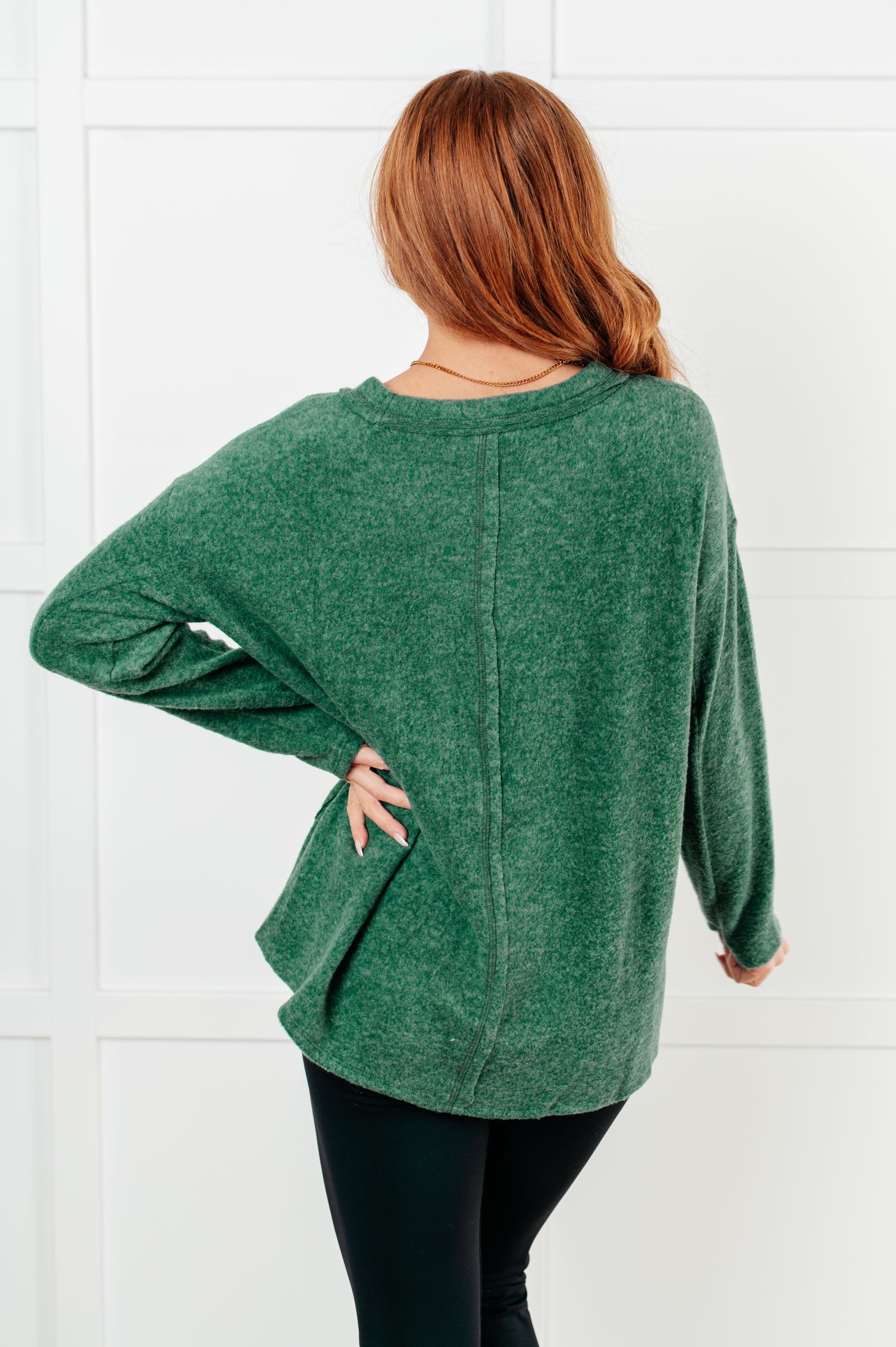 Women's Brushed Hacci Sweater in dark green featuring a round neckline, drop shoulders, stepped hemline, side slits, and raw seams. 