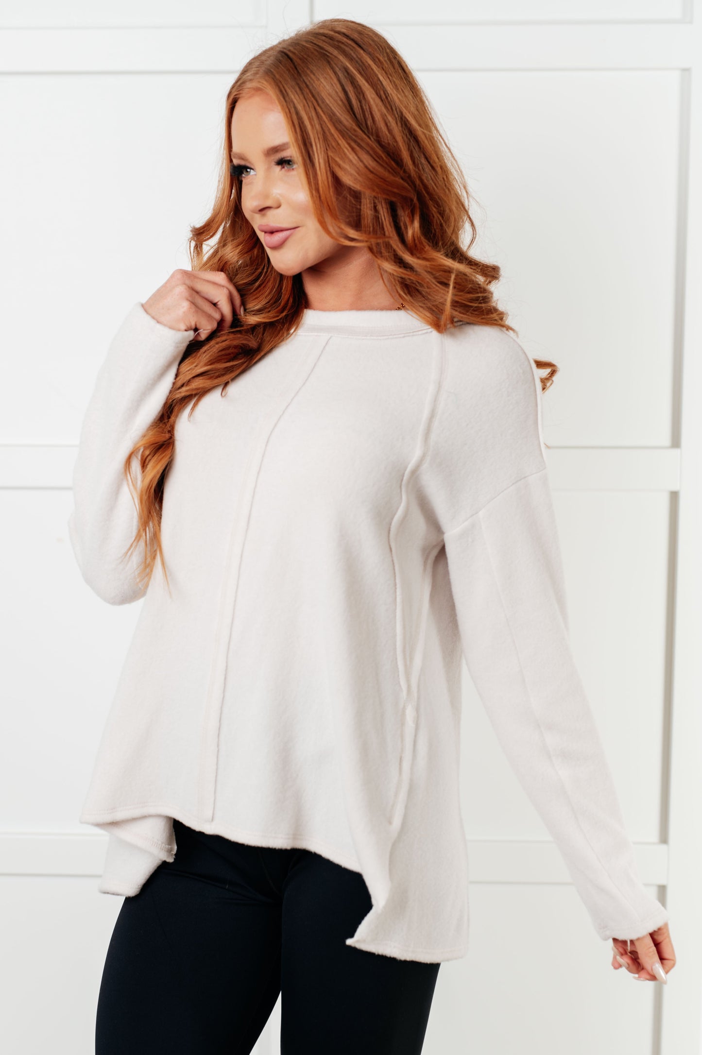 Women's Brushed Hacci Sweater in Sand Beige featuring a round neckline, drop shoulders, stepped hemline, side slits, and raw seams. 