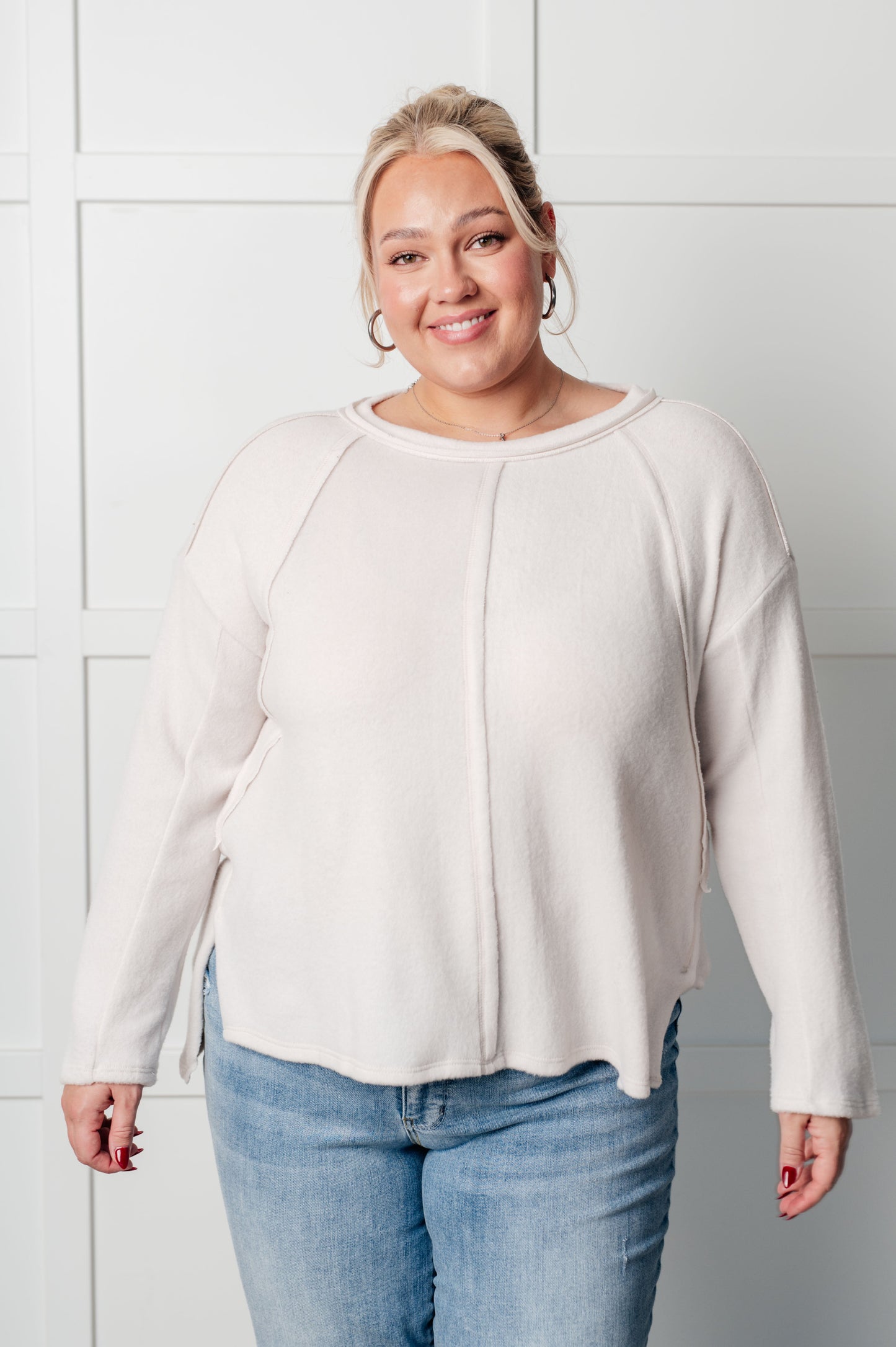 Women's Brushed Hacci Sweater in Sand Beige featuring a round neckline, drop shoulders, stepped hemline, side slits, and raw seams. 