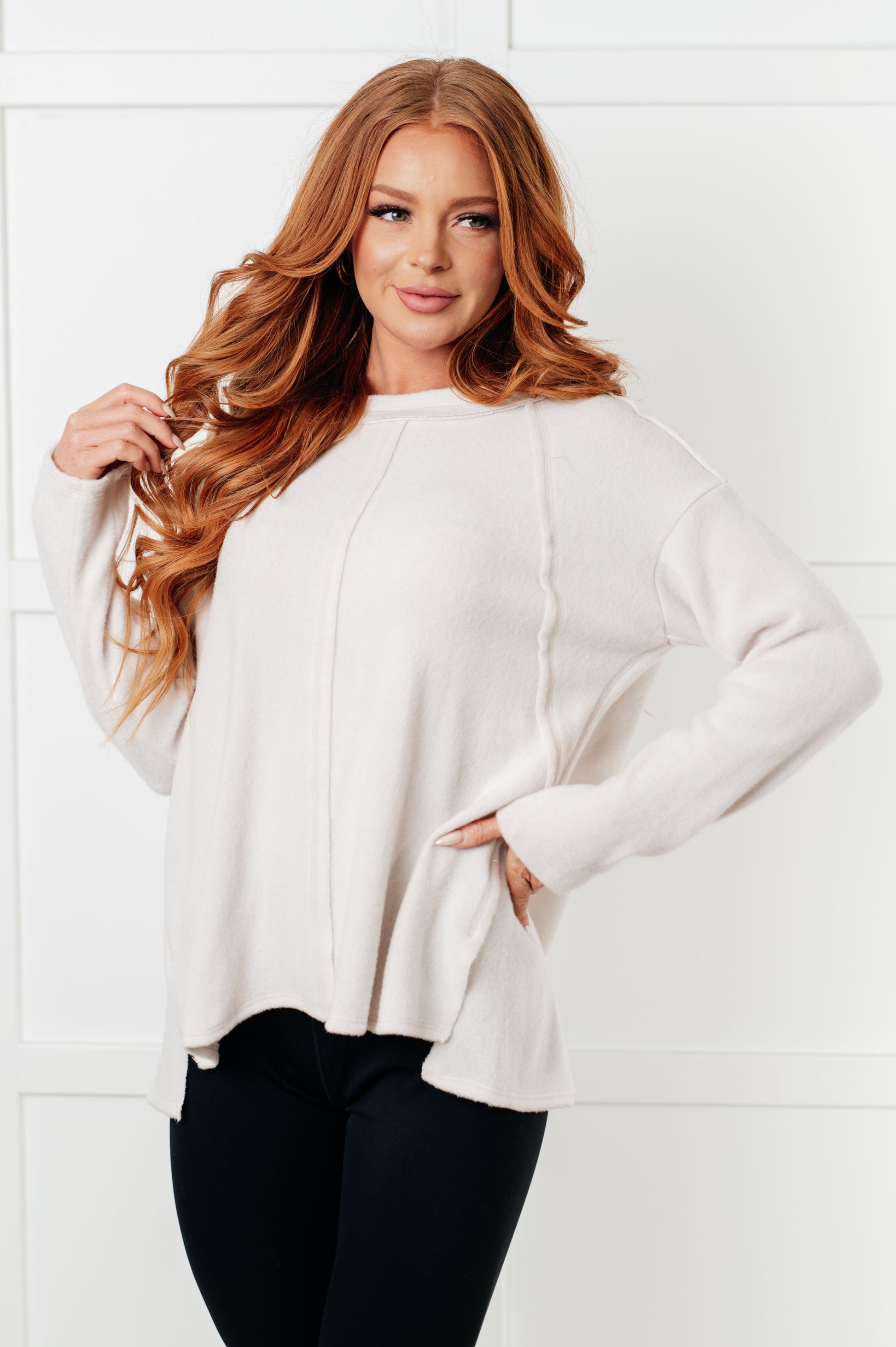 Women's Brushed Hacci Sweater in Sand Beige featuring a round neckline, drop shoulders, stepped hemline, side slits, and raw seams. 