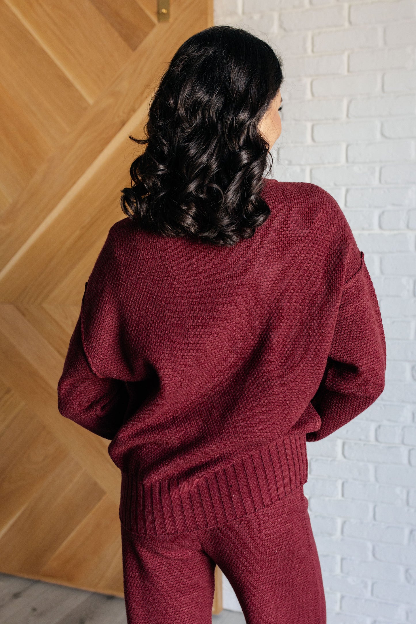 Wine-colored knit set featuring a v-neckline, button-down top with ribbed hem and sleeve cuffs, long sleeves with drop shoulders, and a high-rise jogger fit with a cased elastic ribbed waistline.