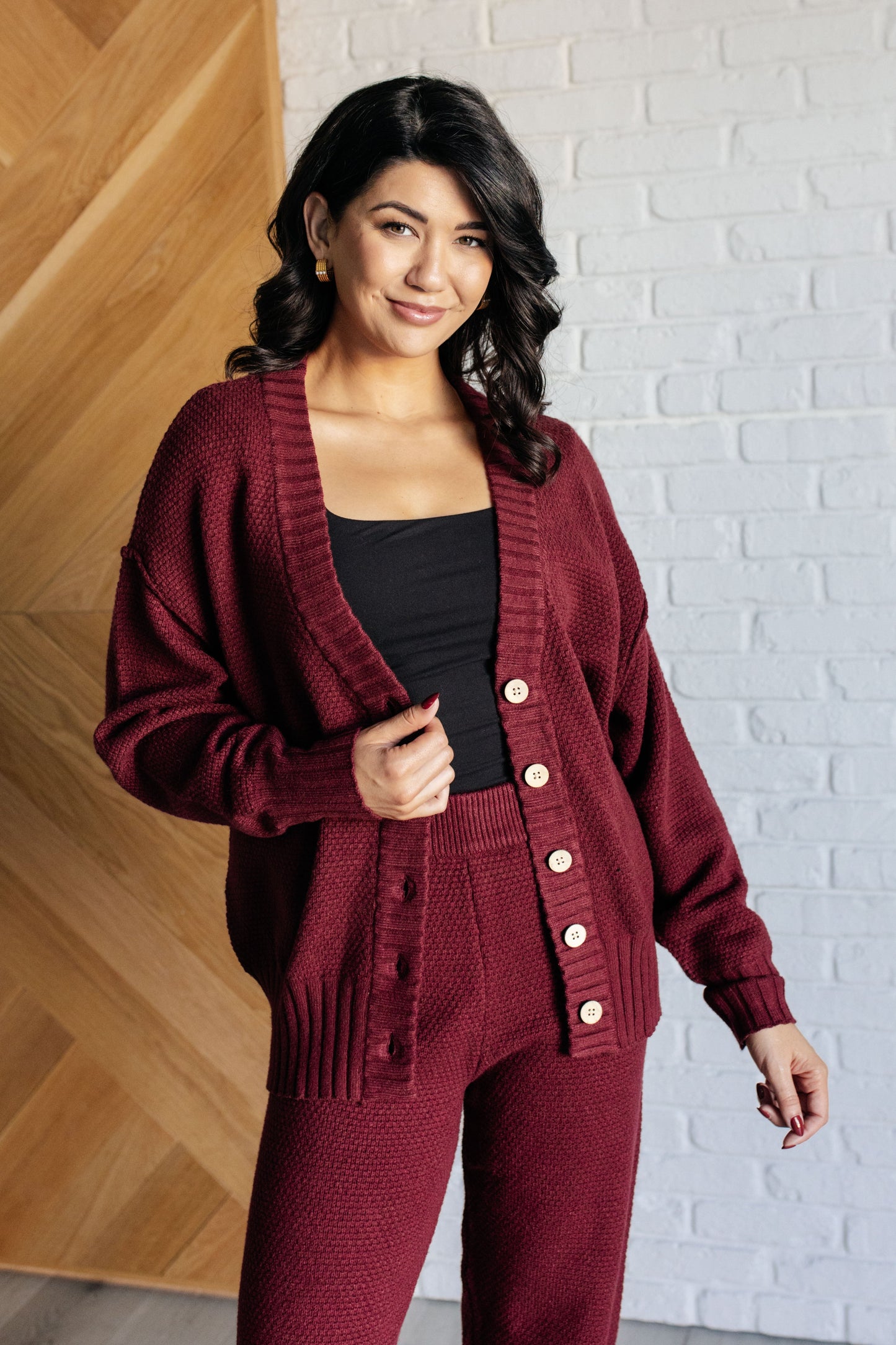 Wine-colored knit set featuring a v-neckline, button-down top with ribbed hem and sleeve cuffs, long sleeves with drop shoulders, and a high-rise jogger fit with a cased elastic ribbed waistline.