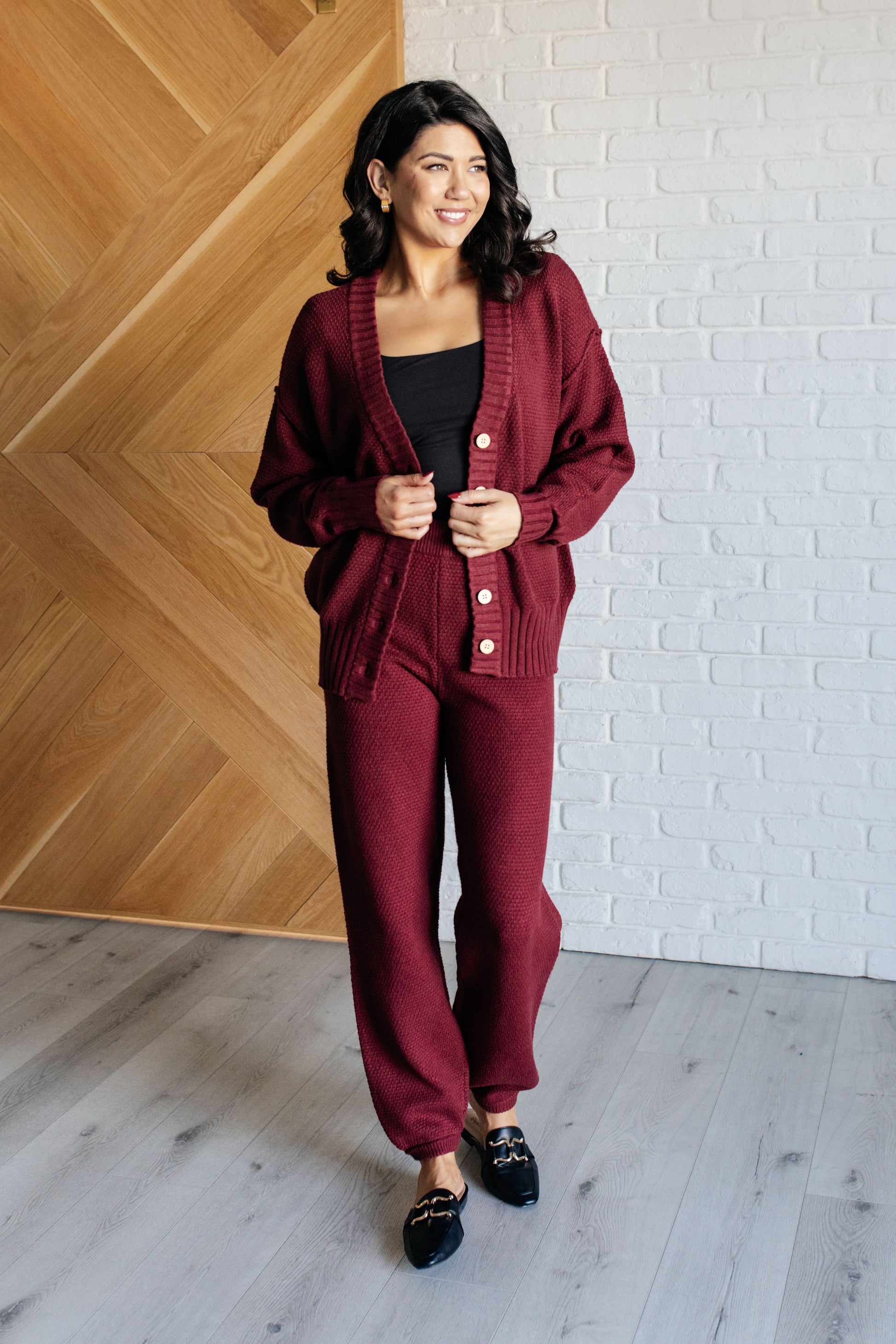 Wine-colored knit set featuring a v-neckline, button-down top with ribbed hem and sleeve cuffs, long sleeves with drop shoulders, and a high-rise jogger fit with a cased elastic ribbed waistline.