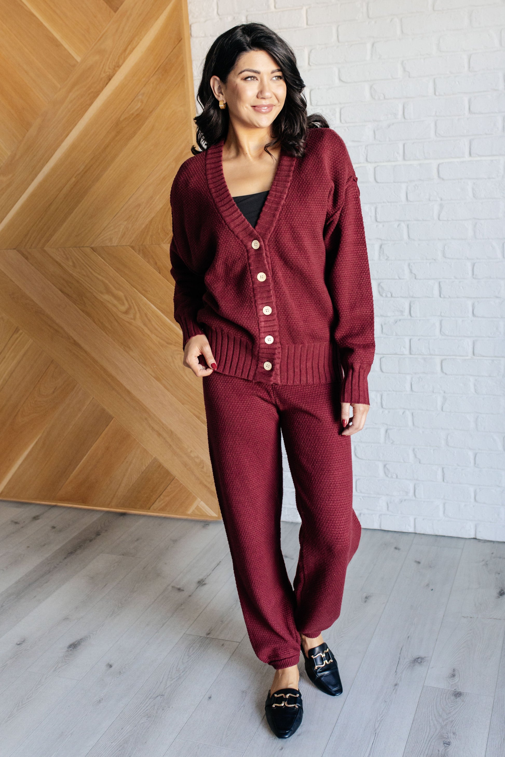 Wine-colored knit set featuring a v-neckline, button-down top with ribbed hem and sleeve cuffs, long sleeves with drop shoulders, and a high-rise jogger fit with a cased elastic ribbed waistline.