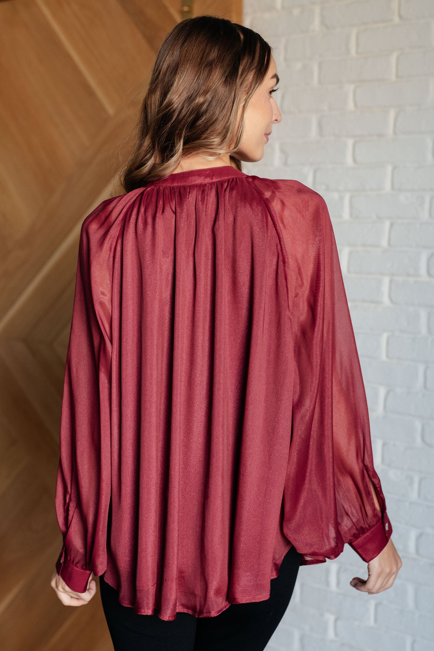 Dark plum chiffon top with a round neckline, long bat sleeves, and banded buttoned sleeve cuffs. Features a front button closure, scooped hem, and a lined bodice.