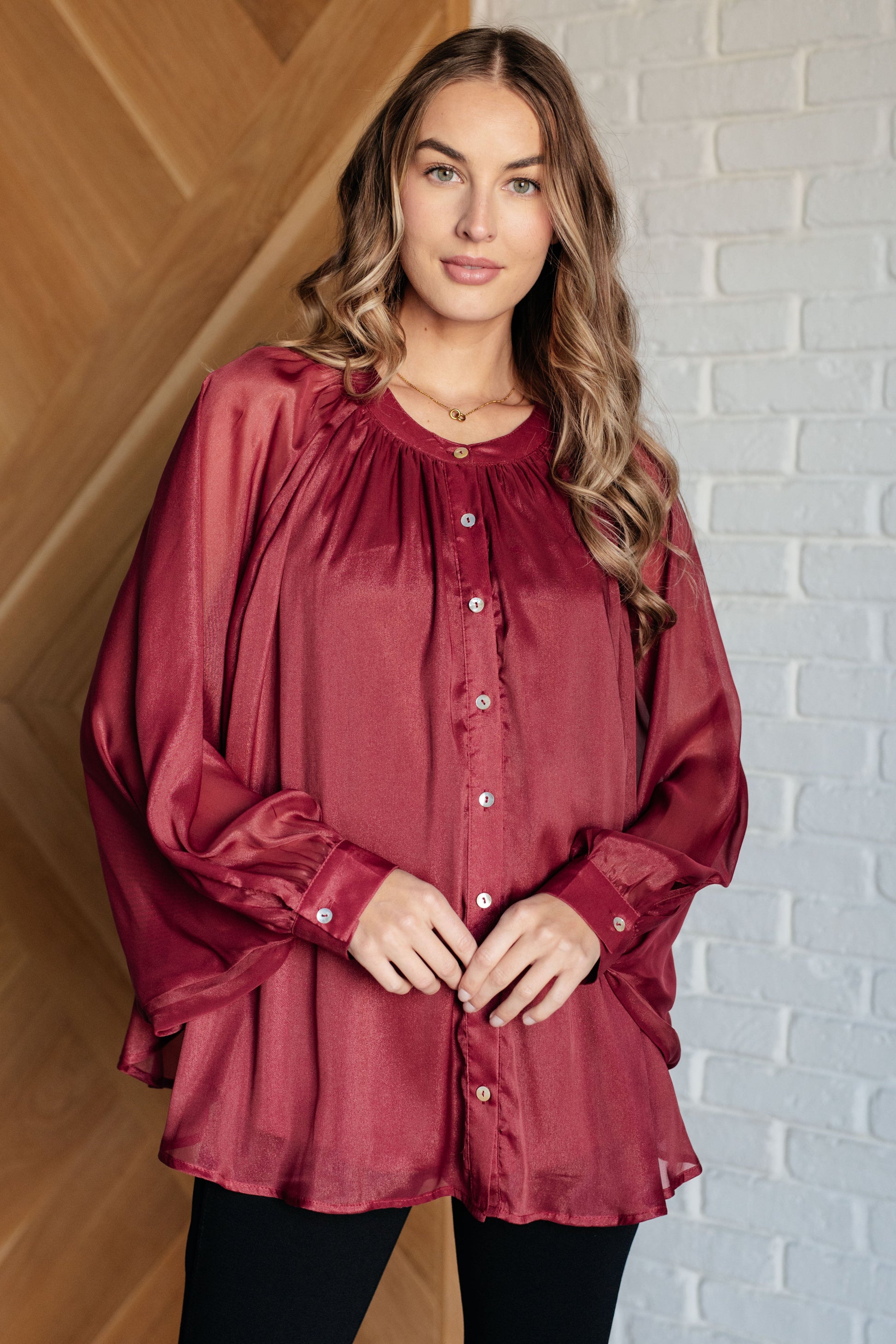 Dark plum chiffon top with a round neckline, long bat sleeves, and banded buttoned sleeve cuffs. Features a front button closure, scooped hem, and a lined bodice.