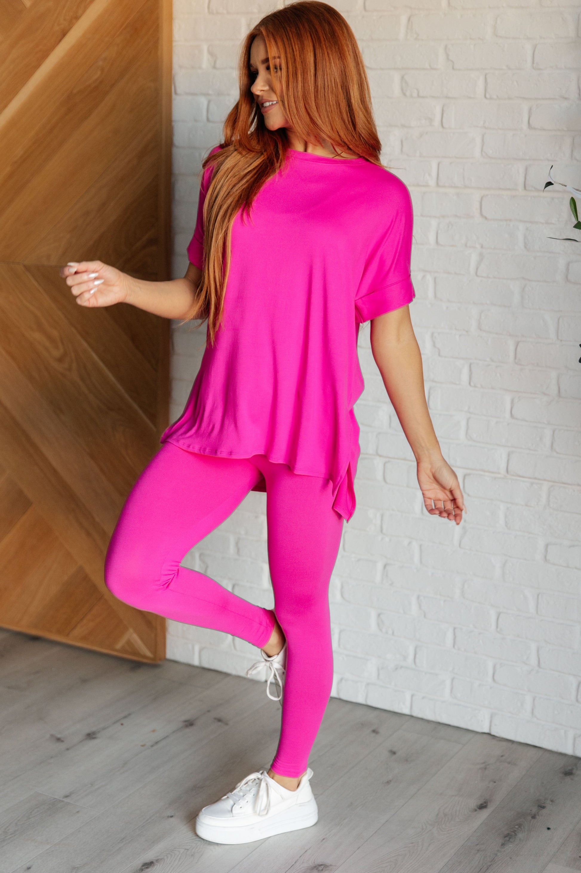 Women's neon hot pink top and leggings set made with brushed microfiber. The top has a round neckline, dolman sleeves, and a high-low hemline with side slits. The leggings have a cased elastic waistline.