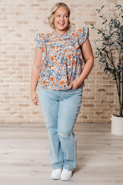 Plus size model wearing Zoe Flutter Sleeve Blouse in orange and blue floral print with jeans and sneakers full body view.