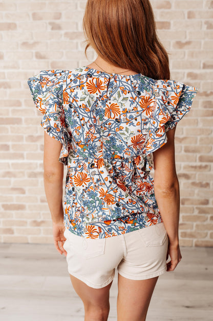 Back view of Zoe Flutter Sleeve Blouse in orange and blue floral print with keyhole closure and layered flutter sleeves.
