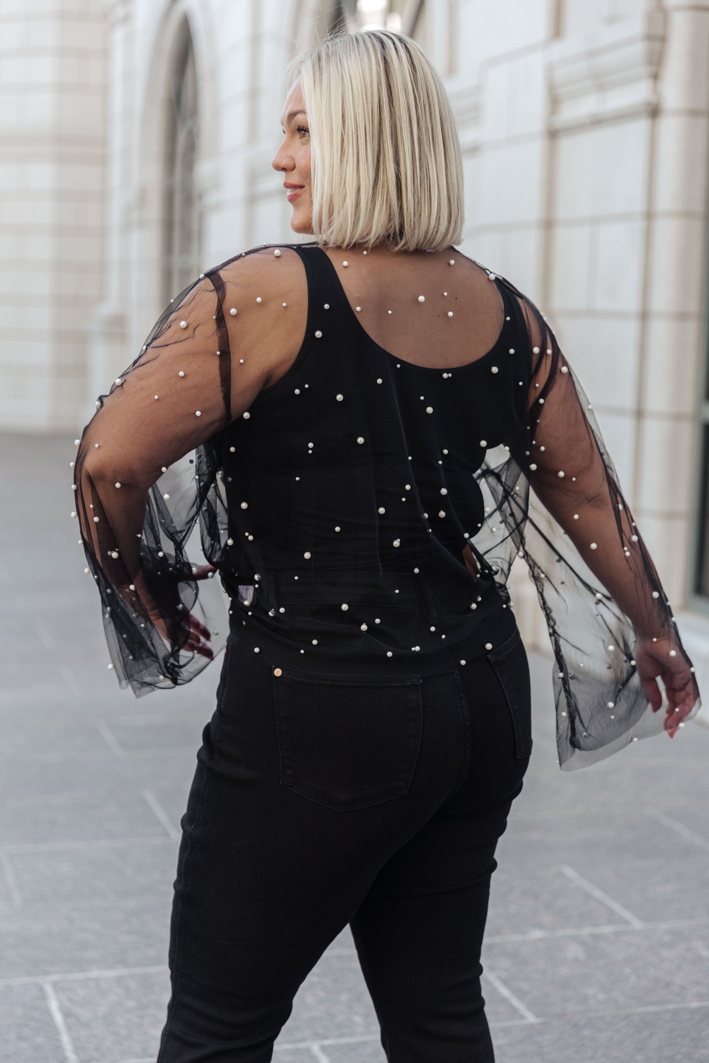 Women's sheer kimono in black mesh with faux pearl embellishments, featuring long flared sleeves, an open front, and an optional self-tie. Perfect for adding a touch of glamour to any outfit.