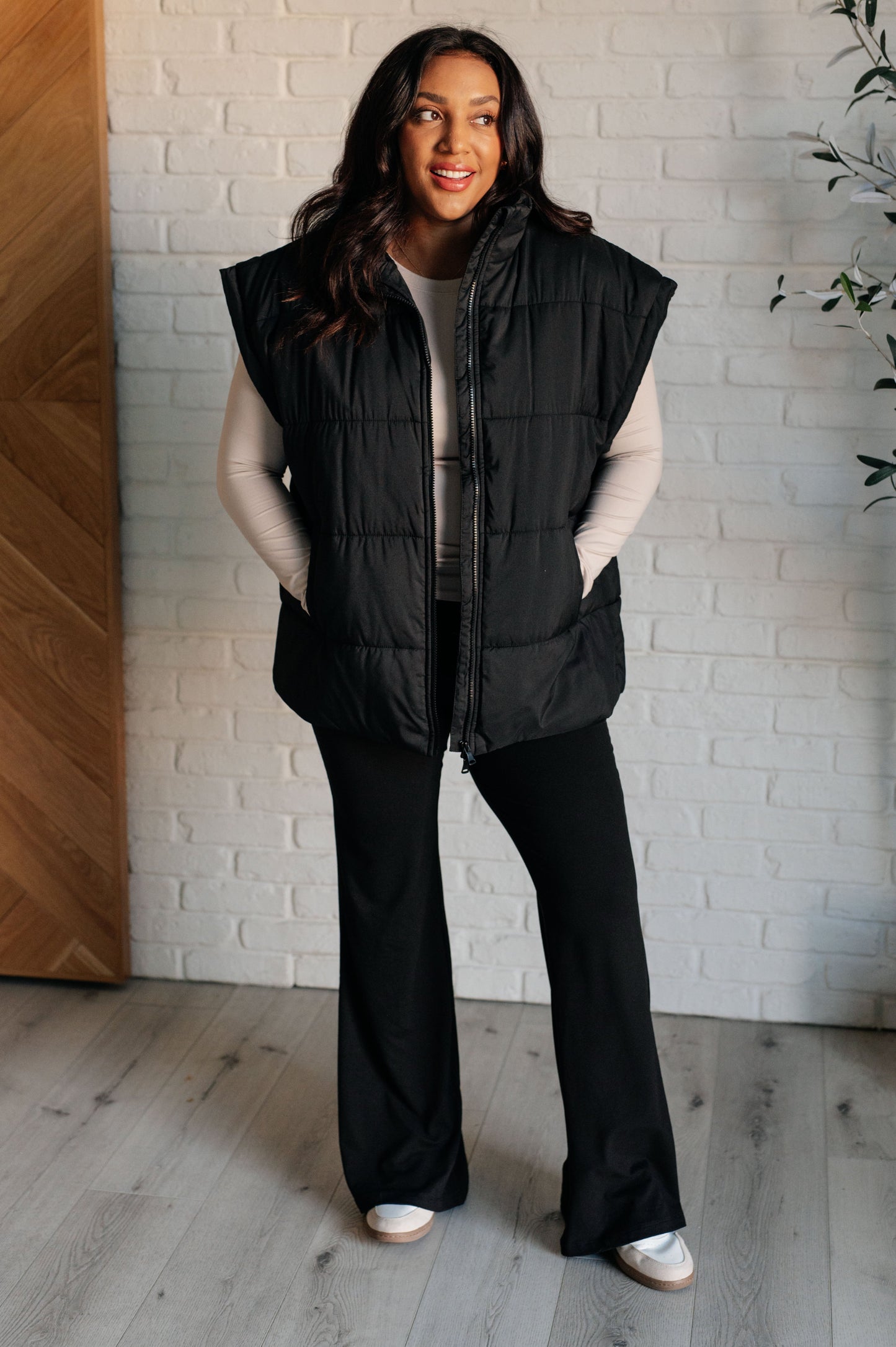 Women's black puffer vest featuring a high neckline, sleeveless design, welt pockets, and a full zipper closure for warmth and style.