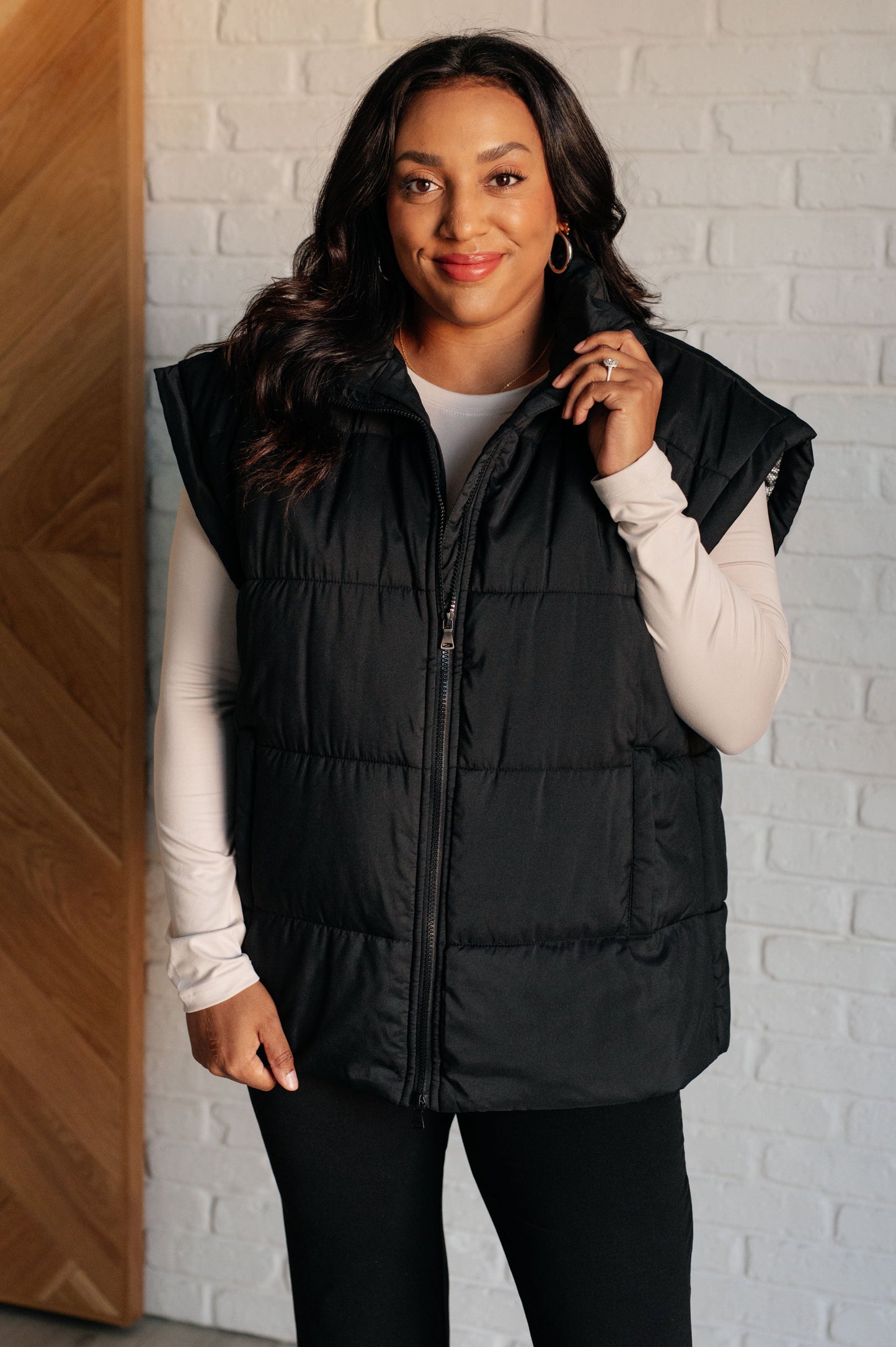 Women's black puffer vest featuring a high neckline, sleeveless design, welt pockets, and a full zipper closure for warmth and style.