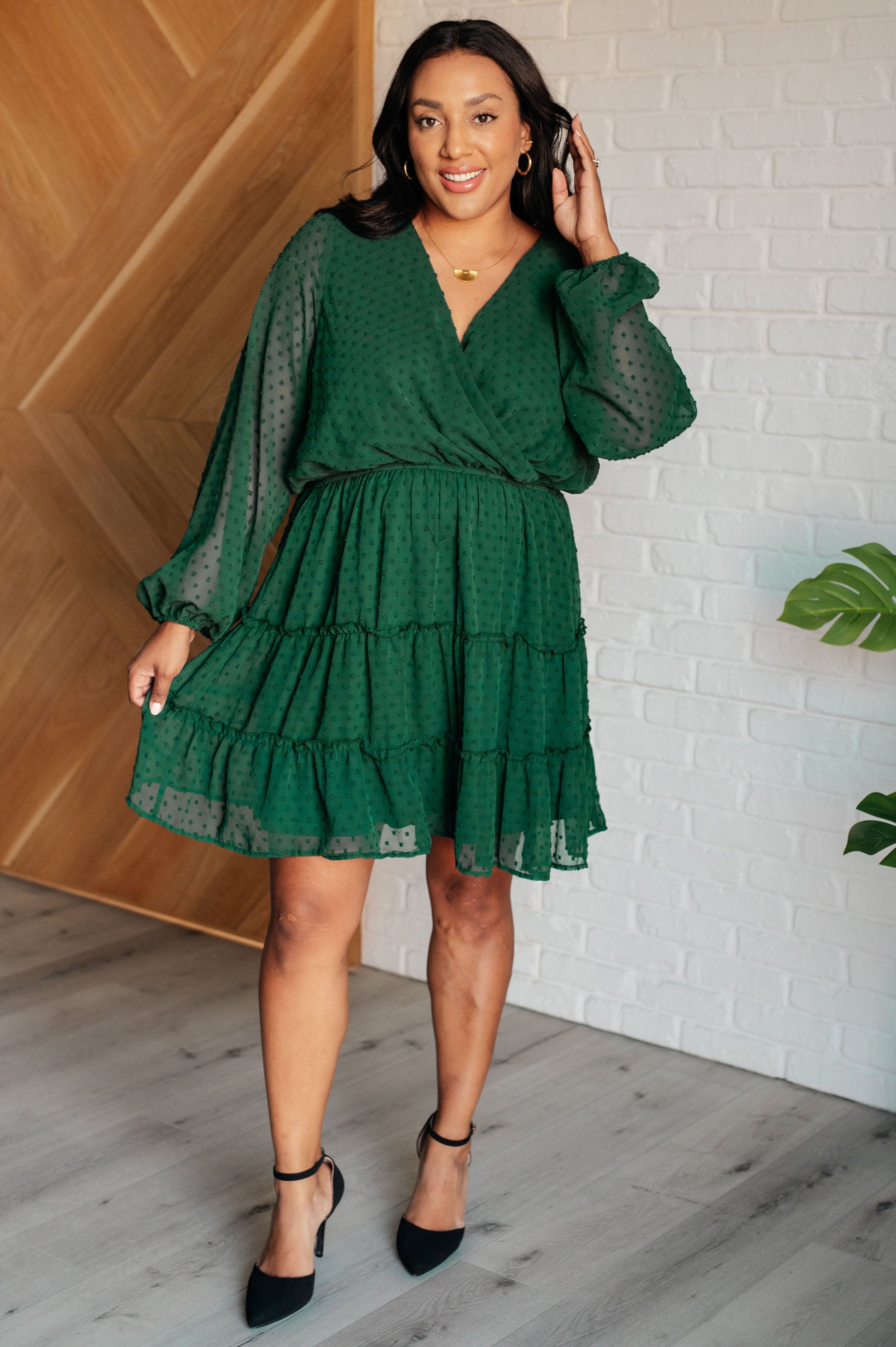 Hunter green V-neck tiered dress made from dot poly chiffon with long balloon sleeves and cased elastic cuffs. Features a surplice bodice, tiered skirt with ruffle details, and a lined skirt and bodice.