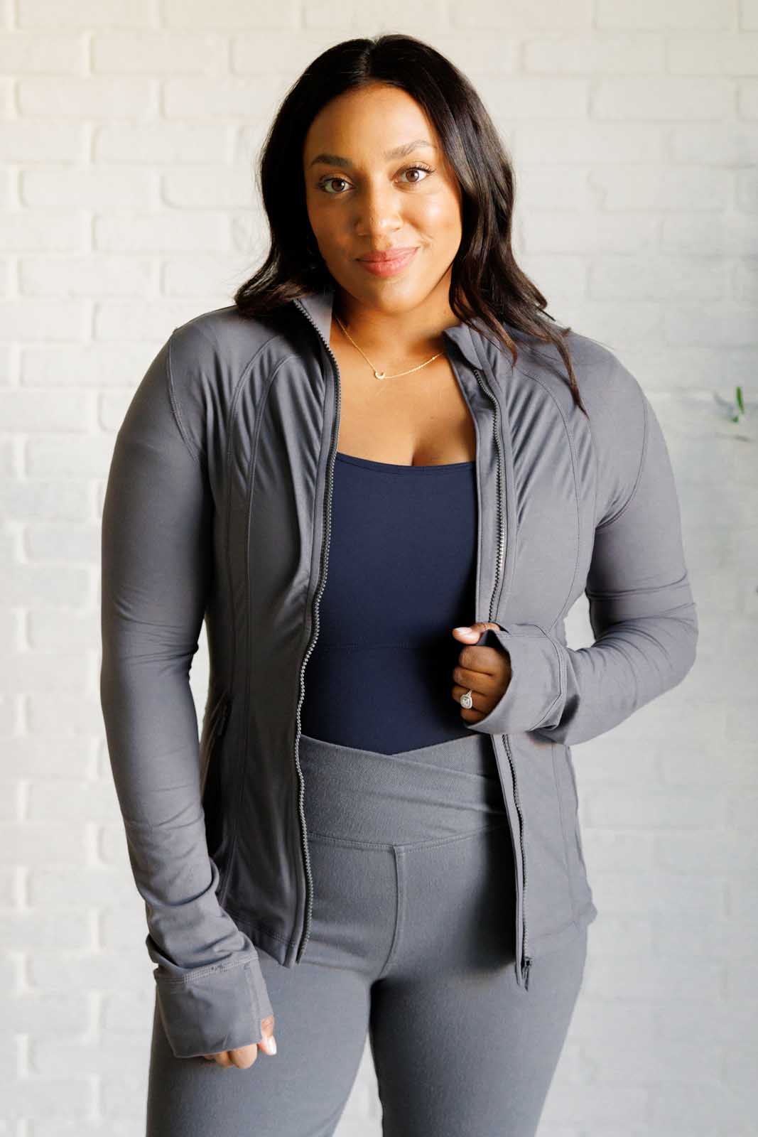 Titanium form-fitting activewear jacket with mock neckline, long sleeves, thumb holes, and a full front zipper. Features back vent and zipper pockets.