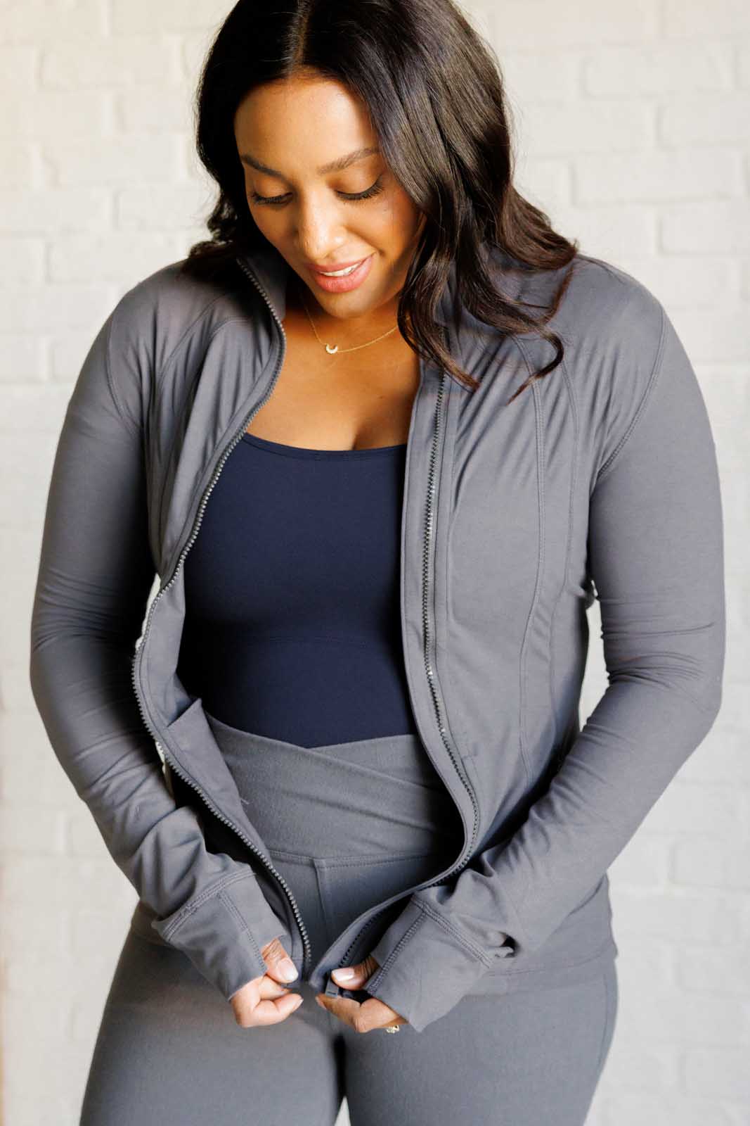 Titanium form-fitting activewear jacket with mock neckline, long sleeves, thumb holes, and a full front zipper. Features back vent and zipper pockets.