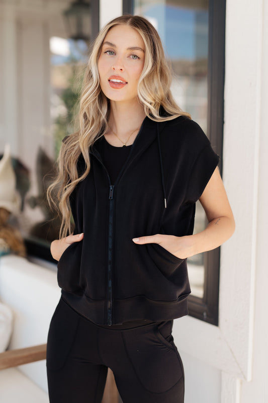 Black sleeveless hoodie with zip front, contour seams, and scoop pockets for sporty-chic comfort.