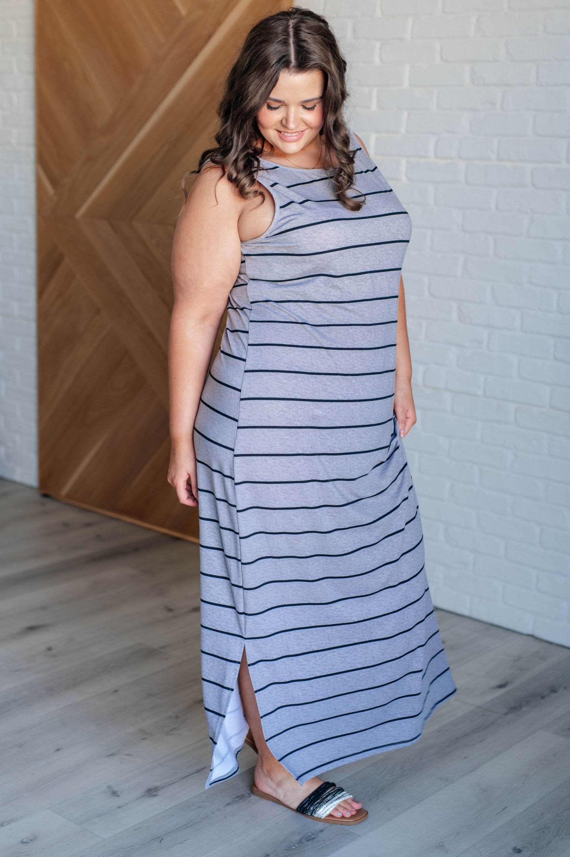 Gray striped sleeveless maxi dress made from mid-weight jersey knit, featuring a scooped neckline and side slits. 