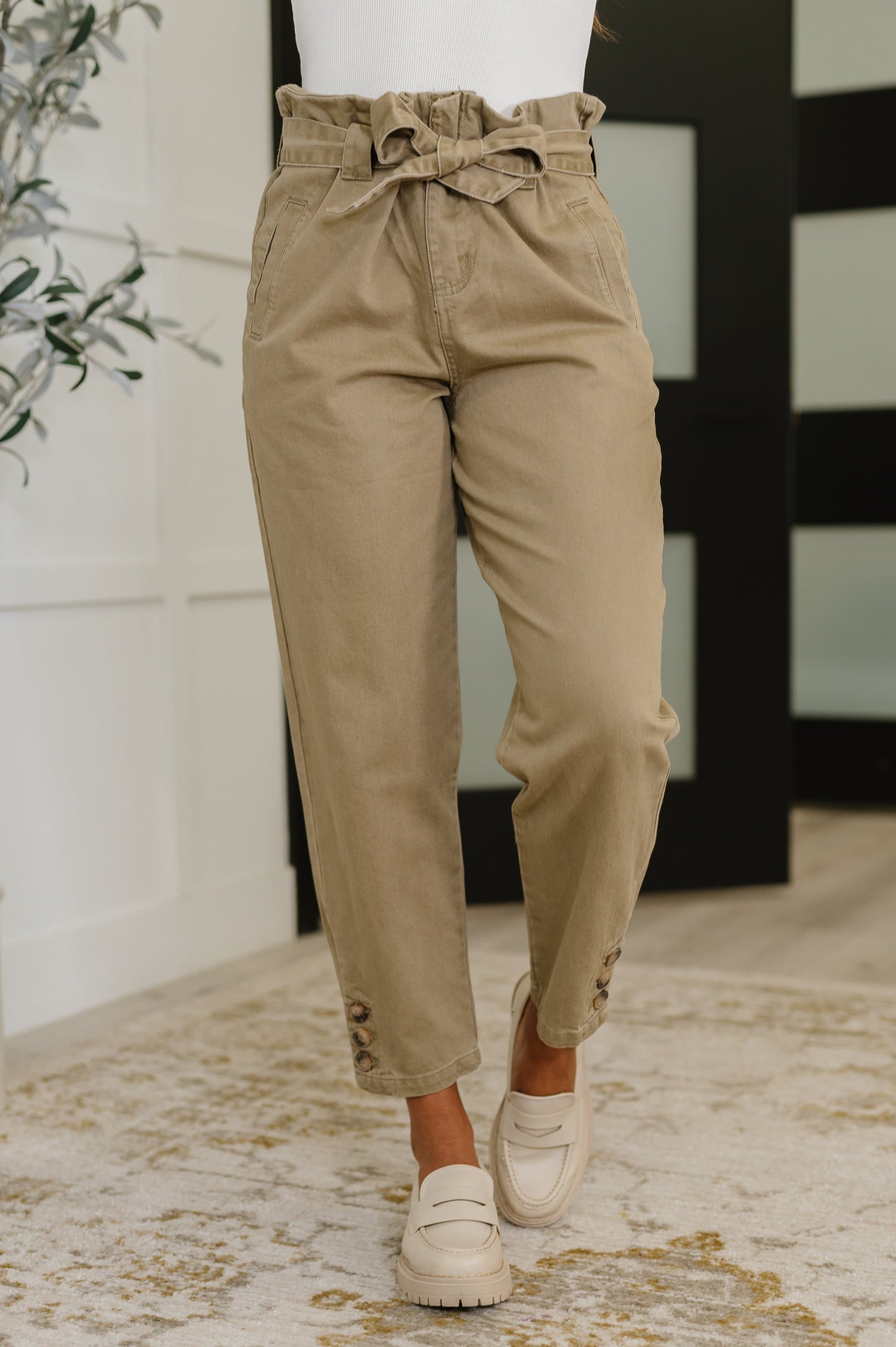 Model wearing Audie High Waist Trousers in beige with paperbag waist and detachable tie belt.
