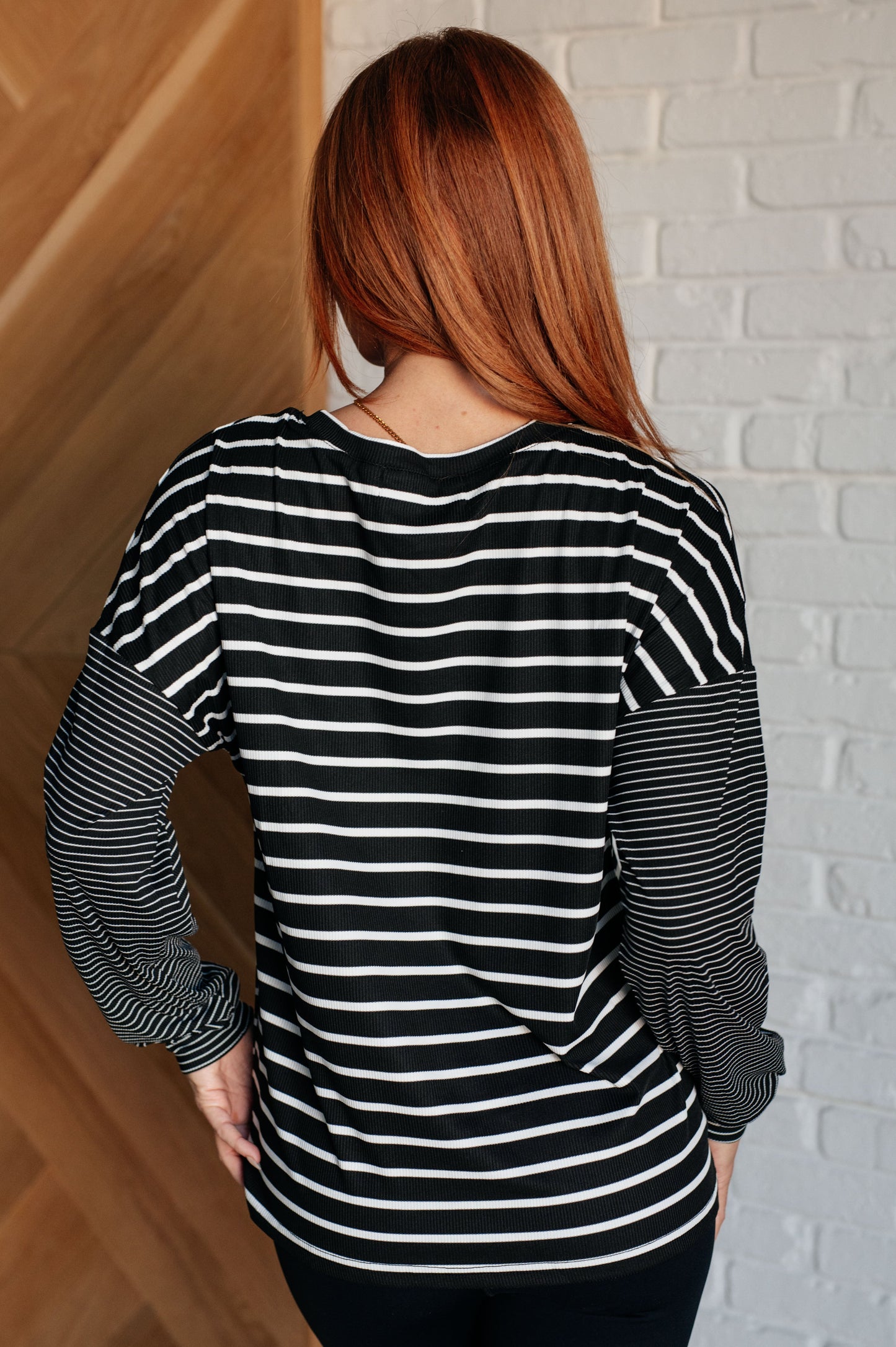 Black and white striped women's top with a round neckline, long drop shoulder sleeves, and banded sleeve cuffs, made from cozy micro ribbed knit fabric.