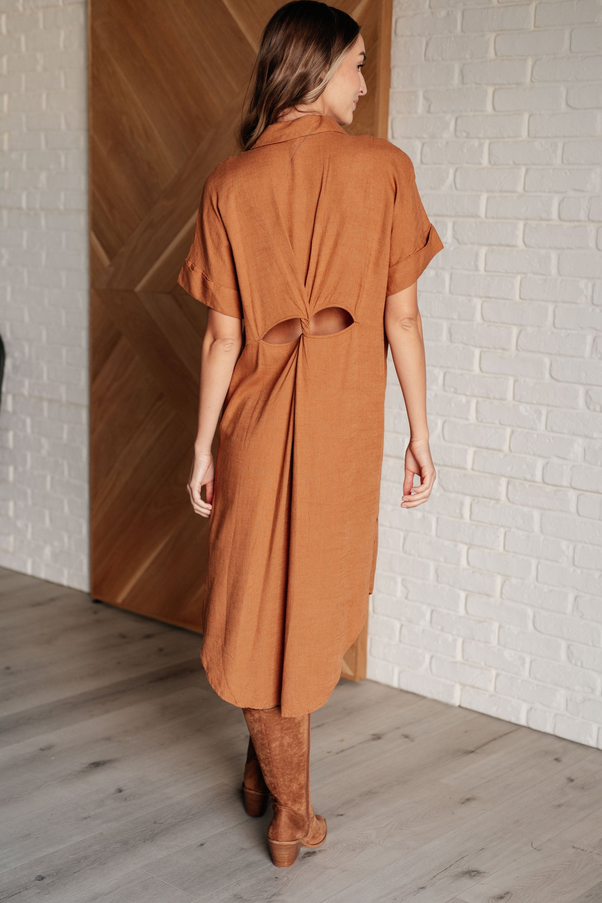 Camel linen blend shirt dress with a collared V-neckline, short dolman sleeves, and tacked sleeve cuffs. Features a button front closure, patch pockets, back cutout detail, side slits, and a scooped hemline.