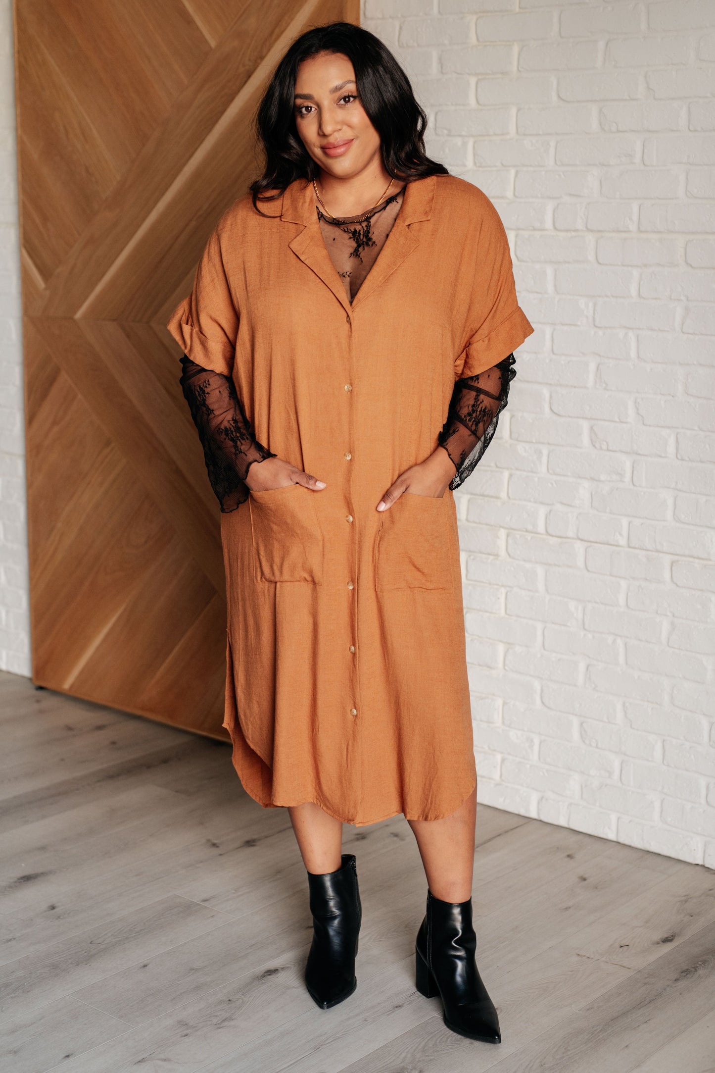 Camel linen blend shirt dress with a collared V-neckline, short dolman sleeves, and tacked sleeve cuffs. Features a button front closure, patch pockets, back cutout detail, side slits, and a scooped hemline.