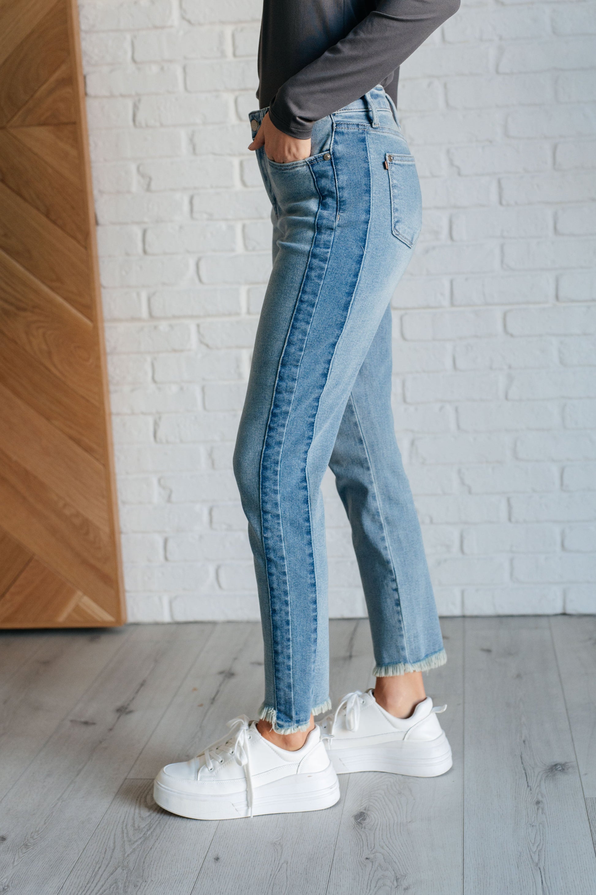 Judy Blue Susan High Rise Slim Jeans in medium wash, featuring contrast side panels, raw frayed hem, high/low stepped hem, and 4-way stretch for a sleek fit.